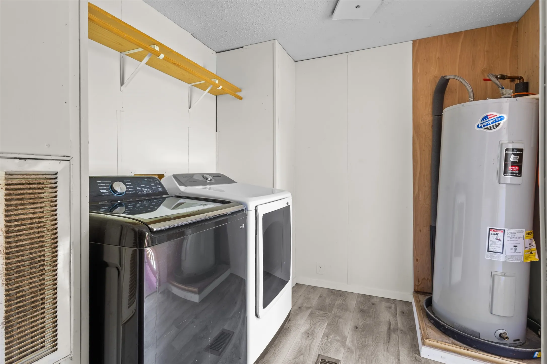 Dedicated laundry area featuring wood-finish flooring, white panel walls, and a built-in water heater