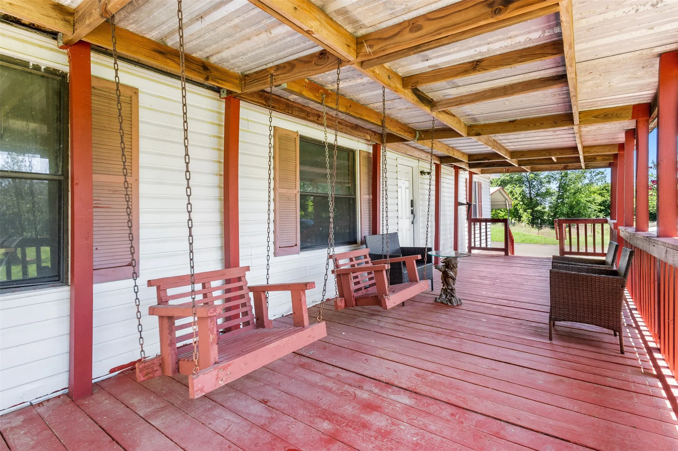 Expansive covered porch featuring a red wood-finish deck, white siding, and exposed wood beam ceiling