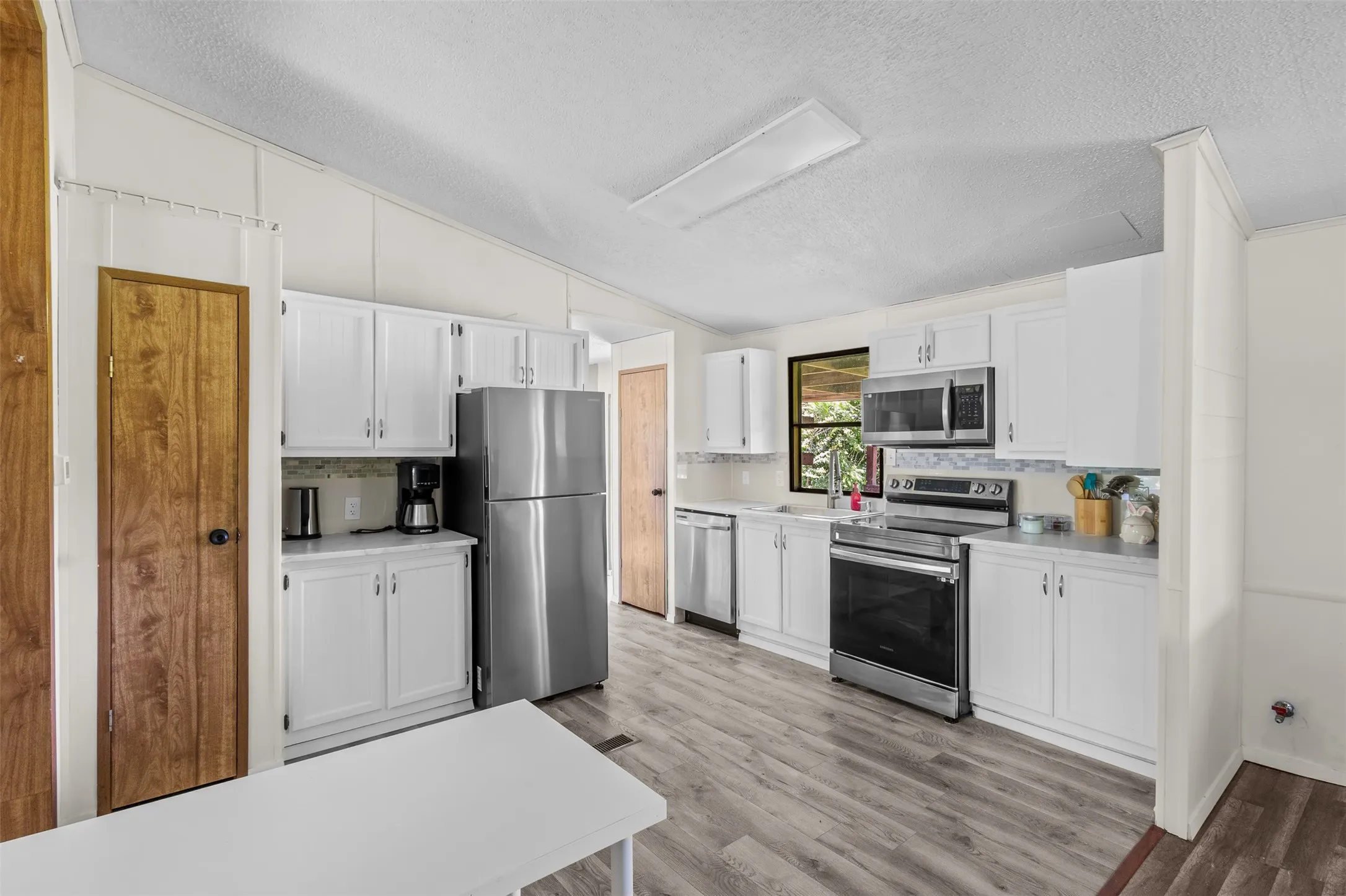 Kitchen featuring white cabinetry, stainless steel appliances, wood-finish flooring, and a tiled backsplash