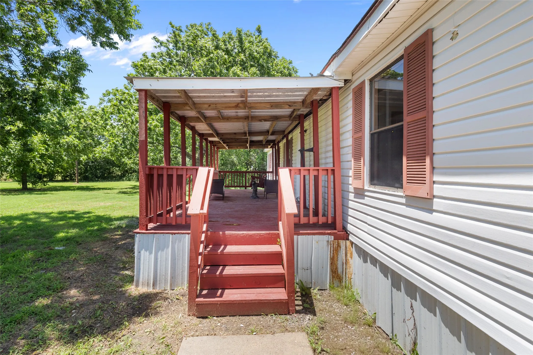 Expansive covered porch featuring wood flooring, red railing, and steps