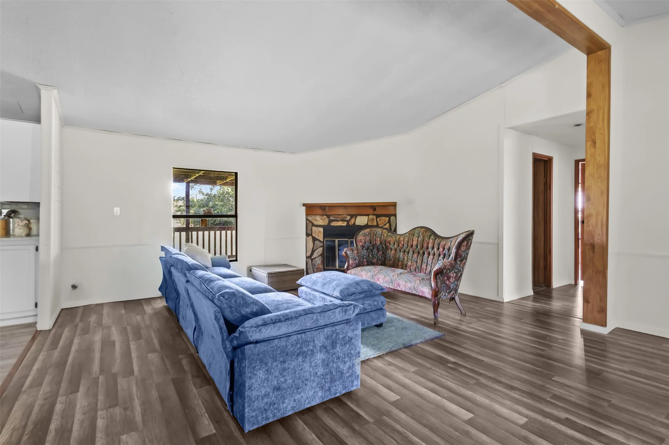 Spacious living area featuring wood-finish flooring, a stone fireplace, and a large window