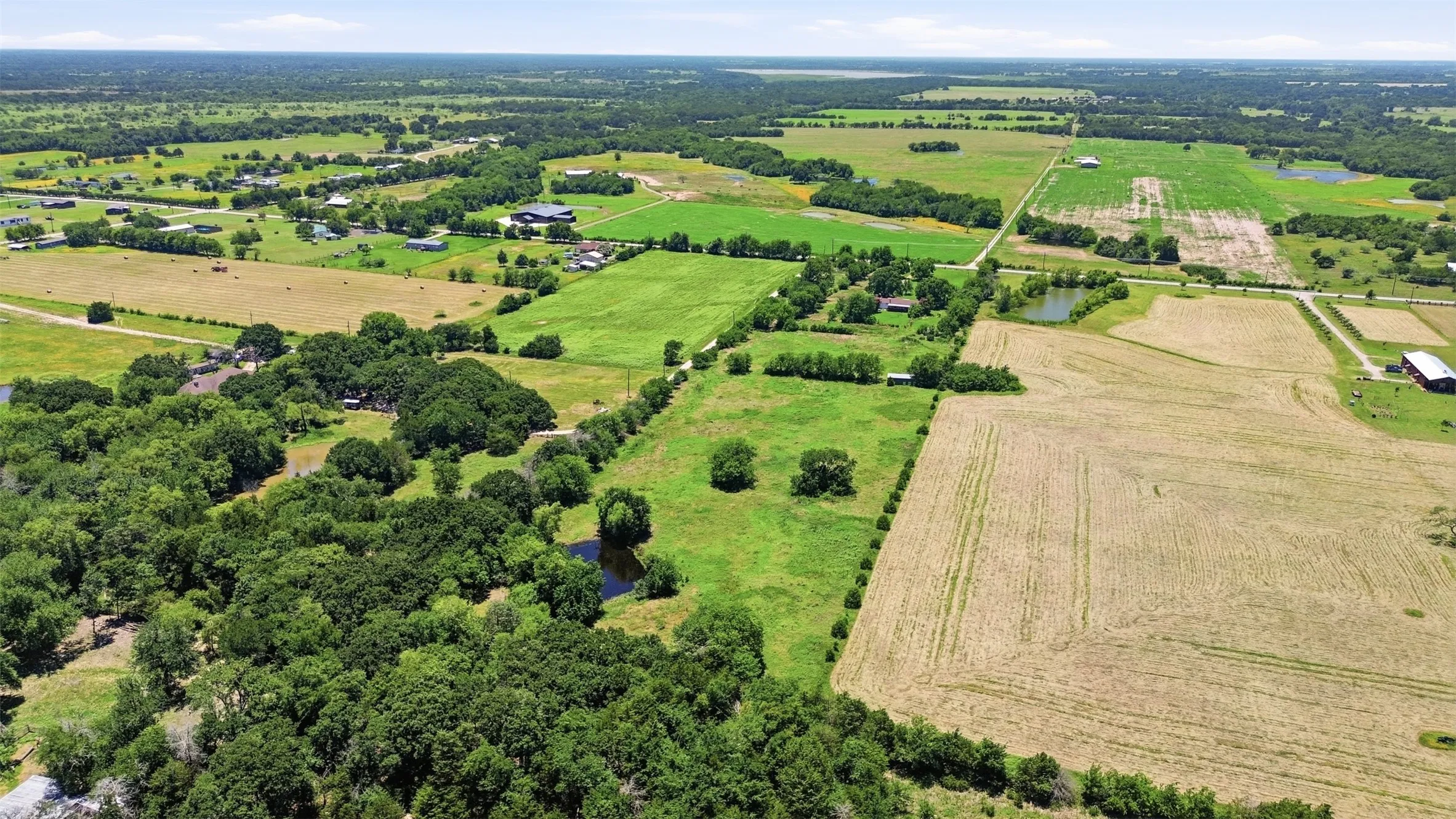 Expansive rural landscape featuring a mix of cultivated fields, green pastures, and dense tree cover
