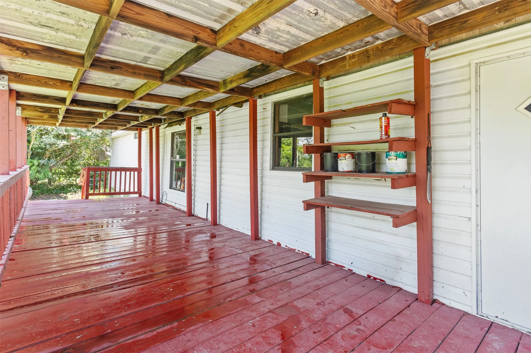 Covered porch area with red-painted wood-finish flooring, white siding, and exposed wooden structural beams