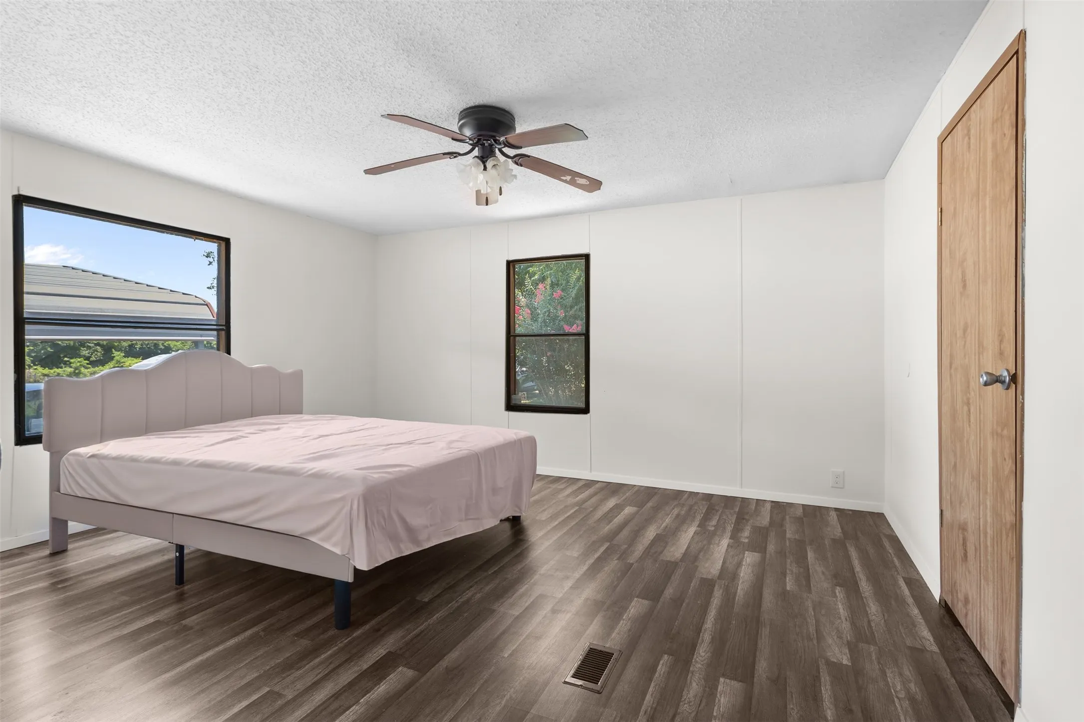 Spacious interior room featuring wood-finish flooring, white panel walls, and a textured ceiling