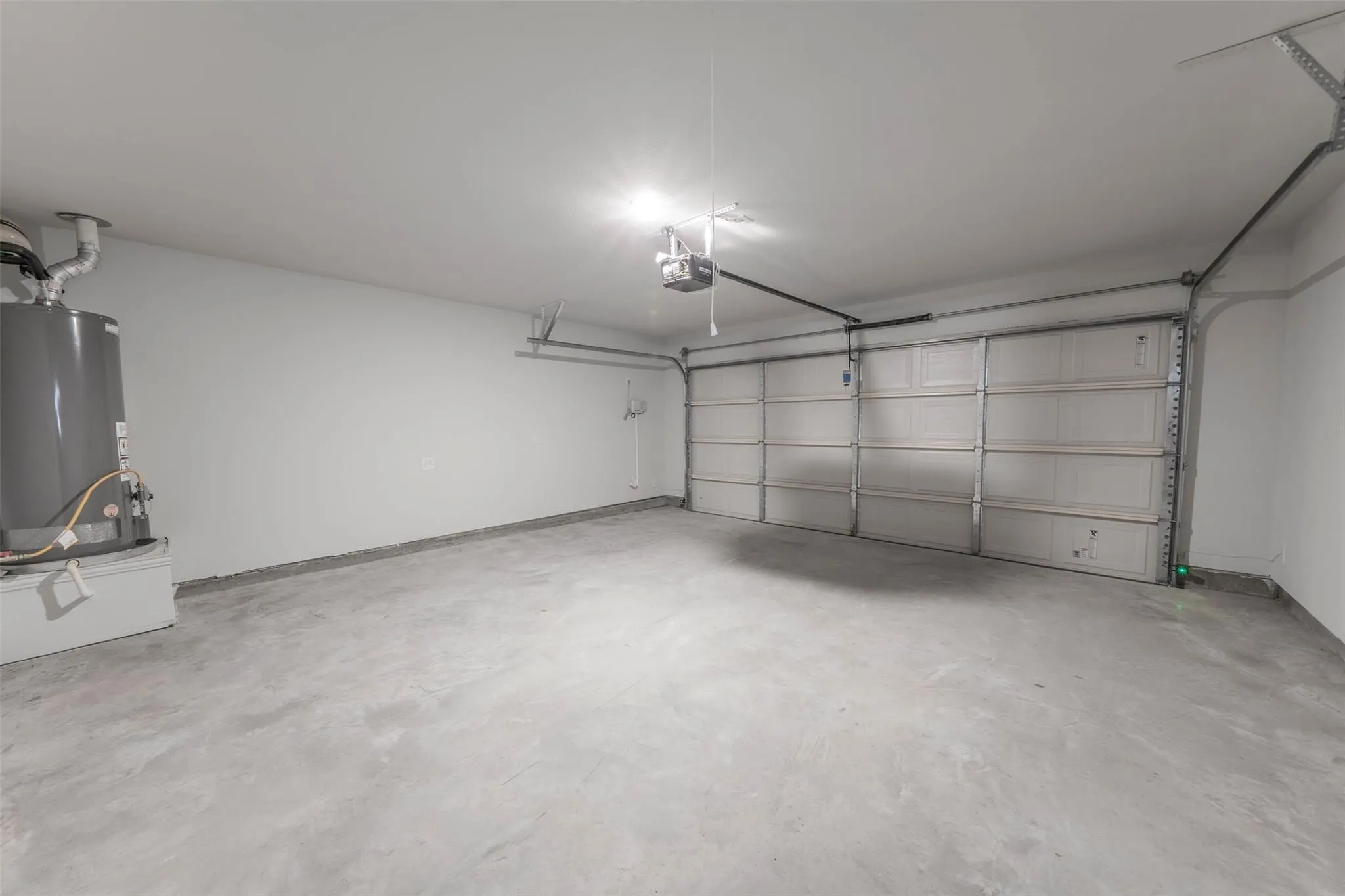 Spacious garage featuring a concrete floor, painted walls, overhead lighting, an automatic garage door opener, and a water heater