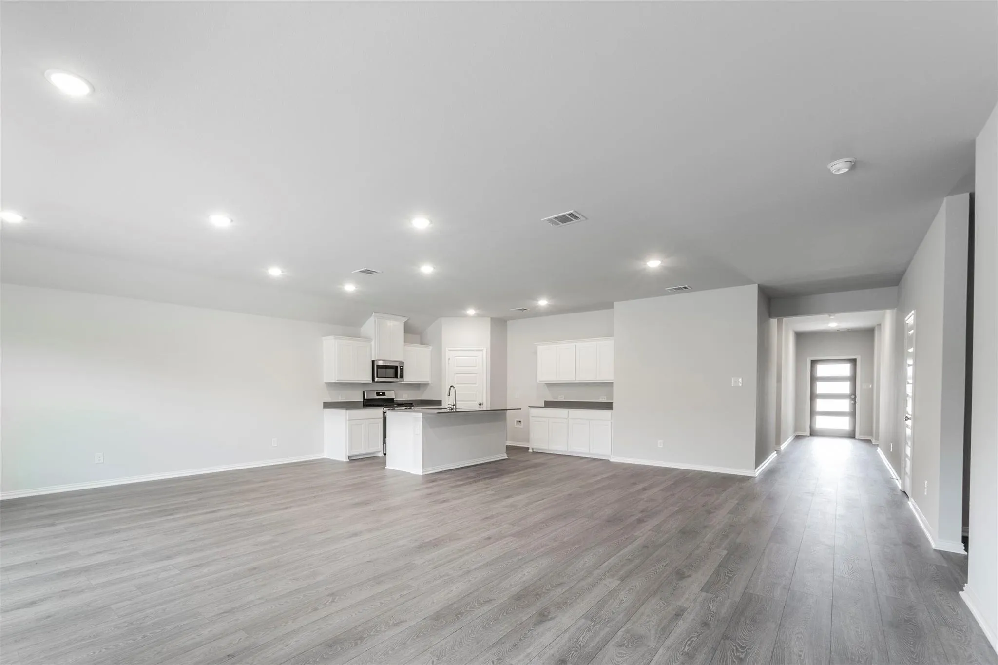 Open-concept living area featuring wood-finish flooring, recessed lighting, and a kitchen with white cabinetry and a central island
