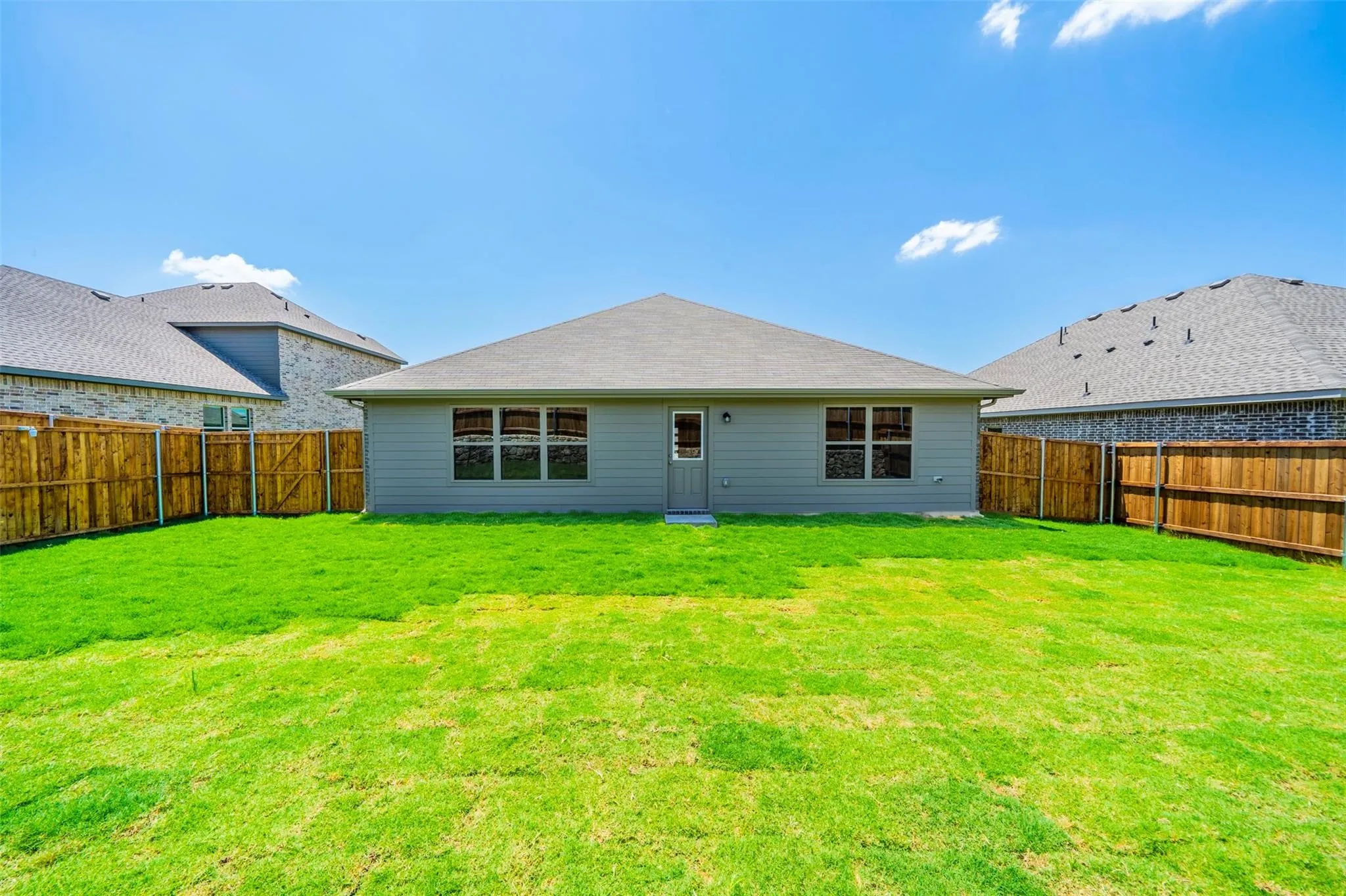 Spacious backyard featuring a manicured lawn, full wood privacy fencing, and a single-story residence with a gray exterior and multiple windows