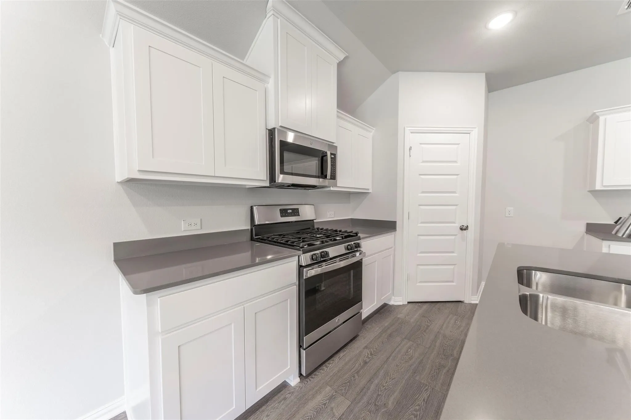 Modern kitchen featuring white shaker cabinetry, stainless steel appliances, gray countertops, a stainless steel sink, and wood-finish flooring