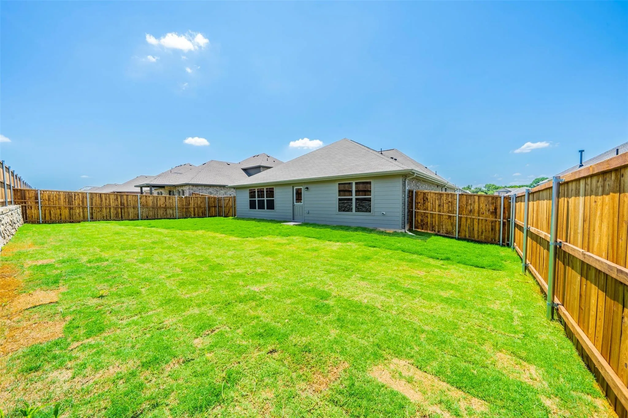 Expansive fenced backyard featuring a manicured lawn, wood privacy fencing, and a light-colored exterior with multiple windows