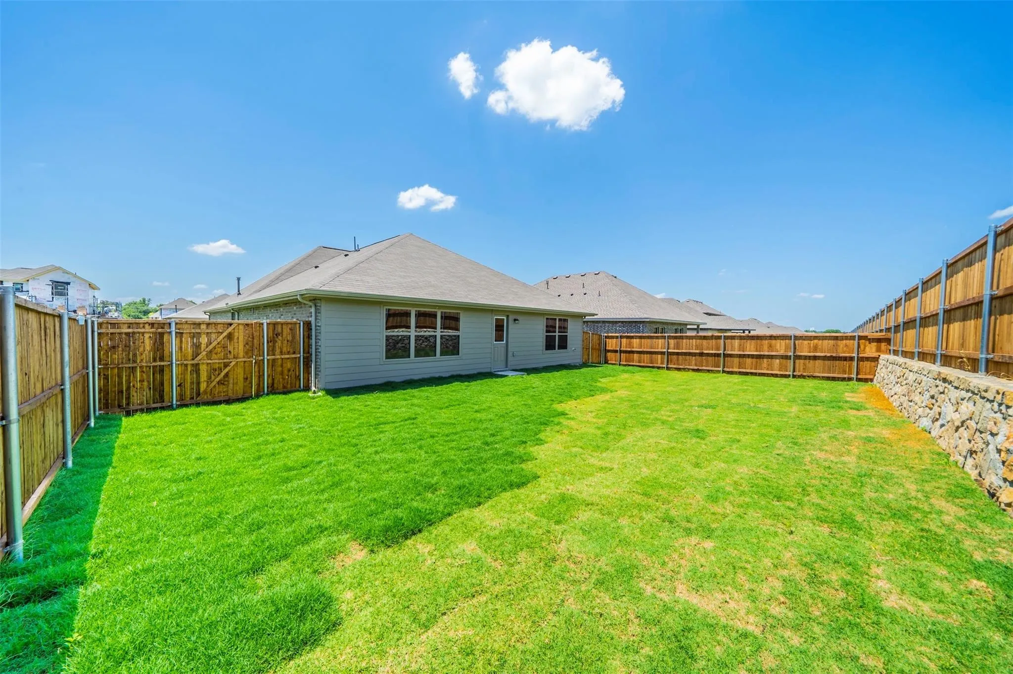 Expansive grassy yard featuring a wood privacy fence and a stone retaining wall