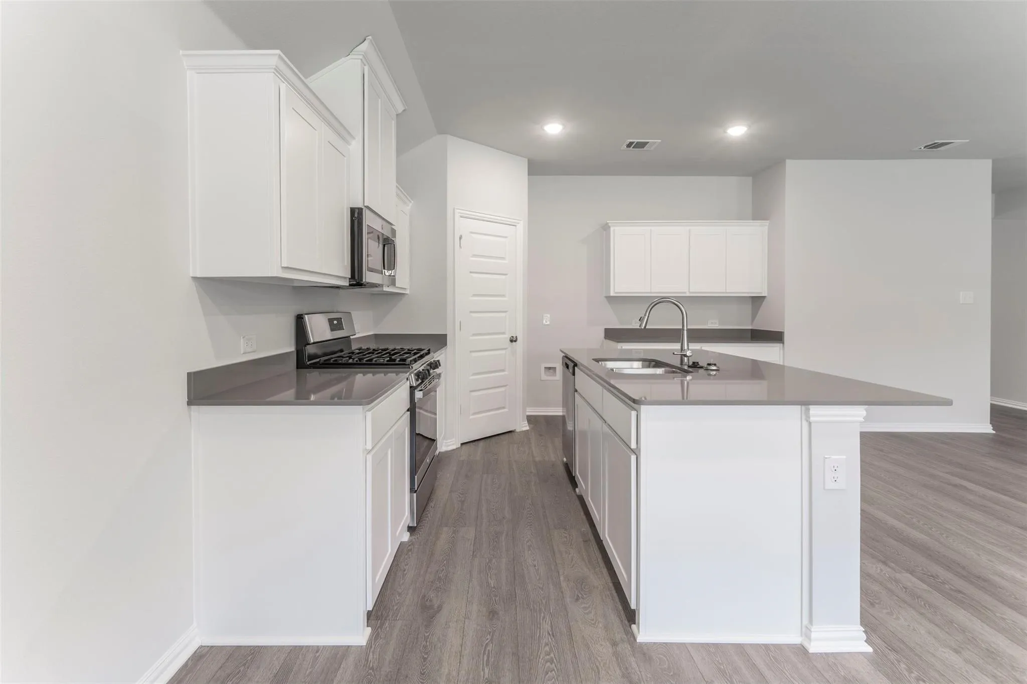 Kitchen featuring white cabinetry, grey countertops, stainless steel appliances, a kitchen island with an undermount sink, and wood-finish flooring