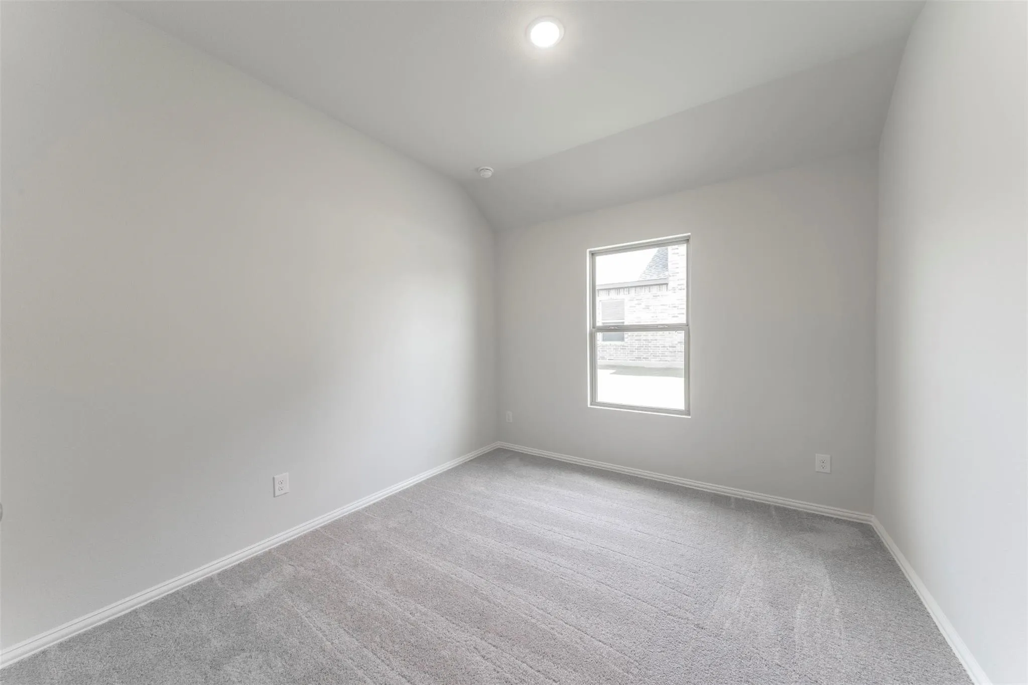 Recessed ceiling lighting illuminates a room featuring light gray walls, gray carpeting, a single window, and white baseboards