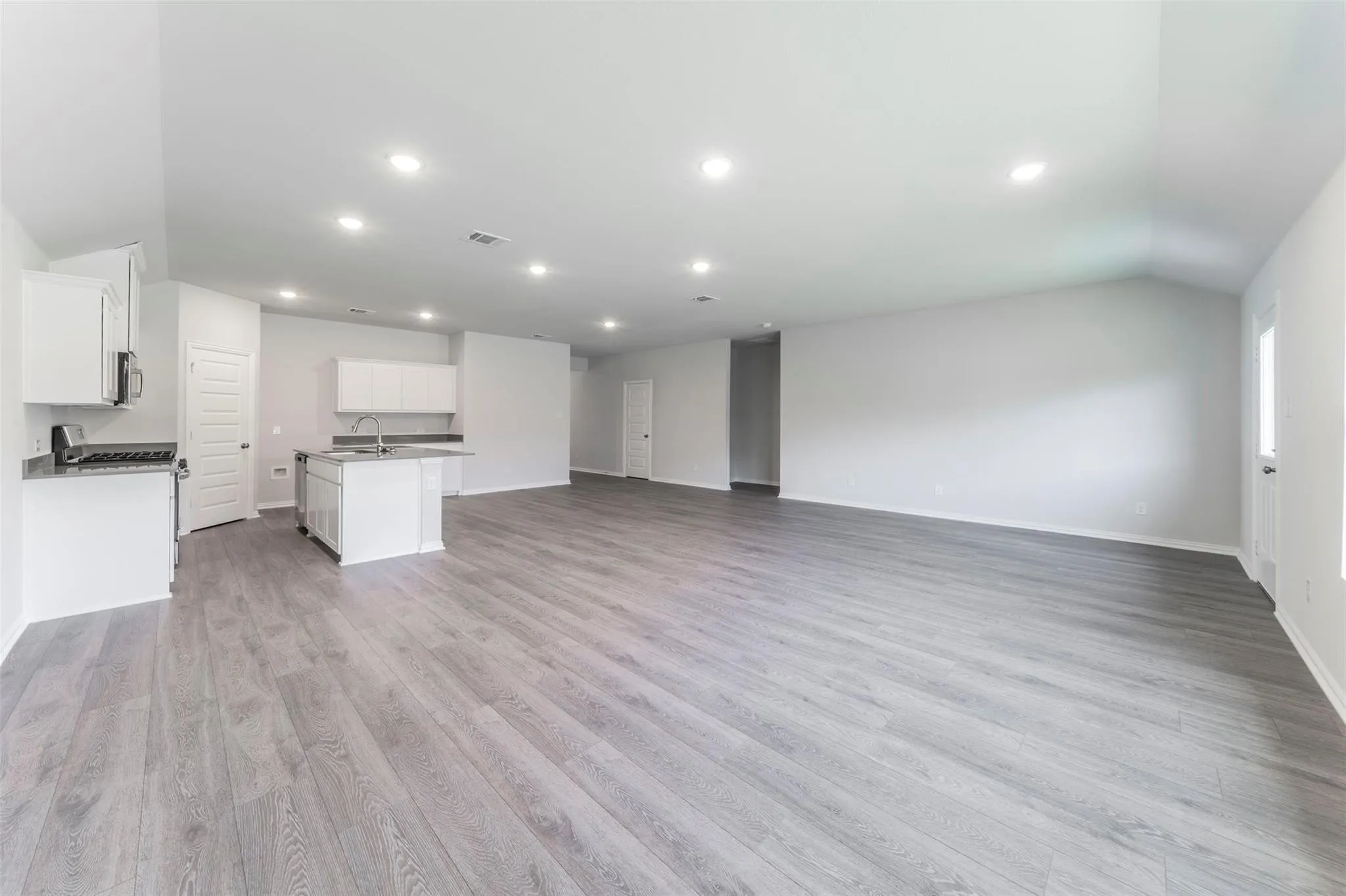 Spacious room featuring wood-finish flooring, recessed lighting, and a kitchen area with white cabinetry and dark countertops