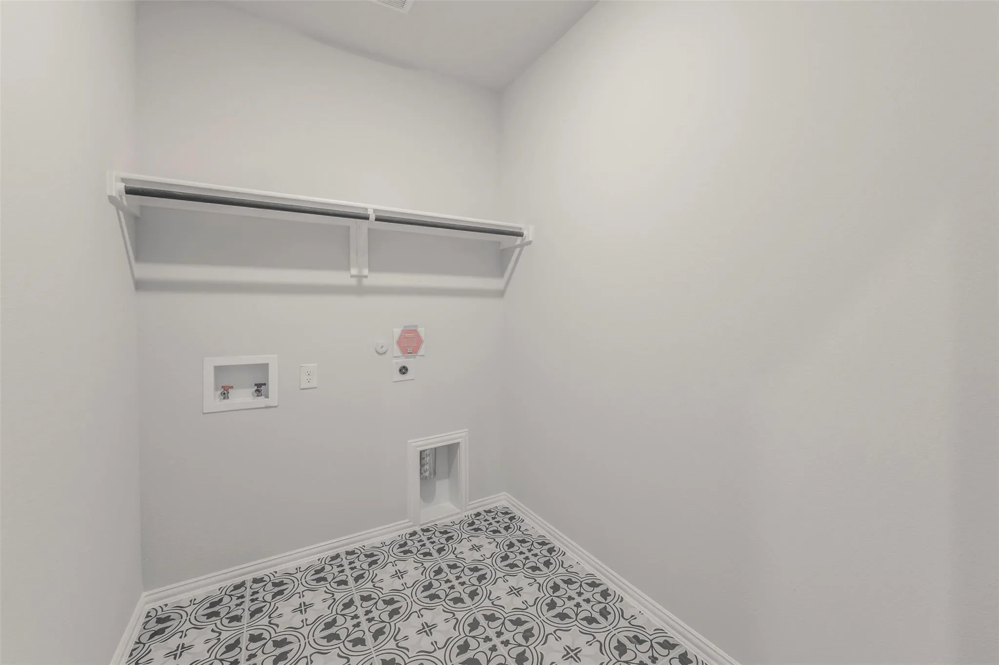 Laundry area featuring patterned floor tiles, white baseboards, and a built-in shelving unit with a hanging rod