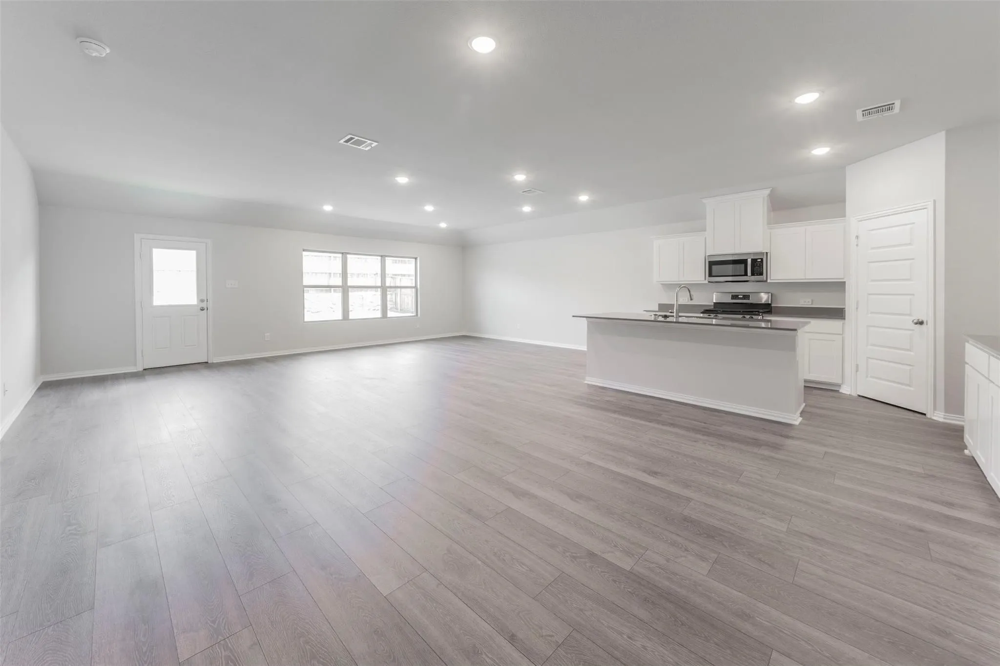Open-concept living space featuring wood-finish flooring, recessed lighting, and multiple windows for natural illumination
