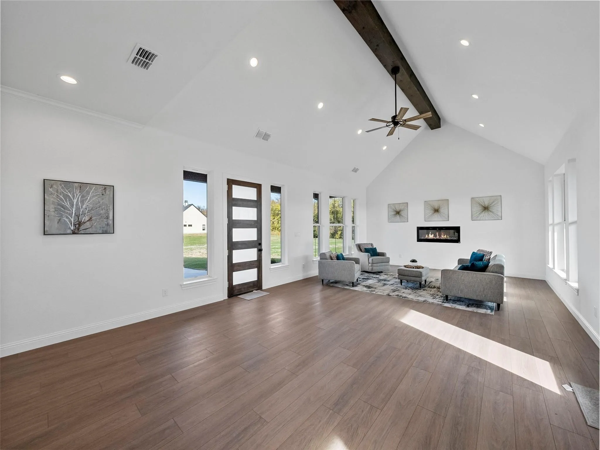 Vaulted ceiling with exposed beam, wood-finish flooring, recessed lighting, linear fireplace, and ceiling fan