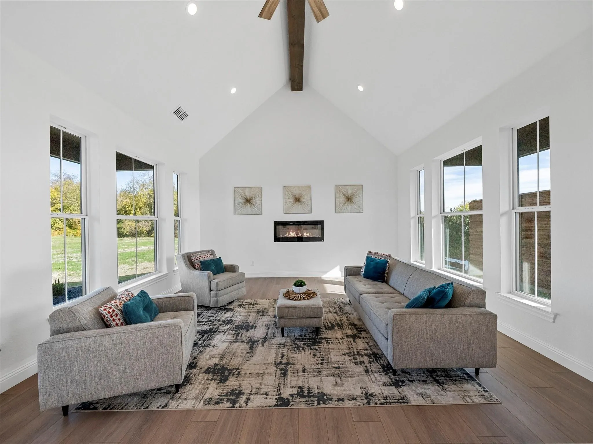Vaulted ceiling with exposed wood beam, recessed lighting, wood-finish flooring, built-in fireplace, and multiple tall windows