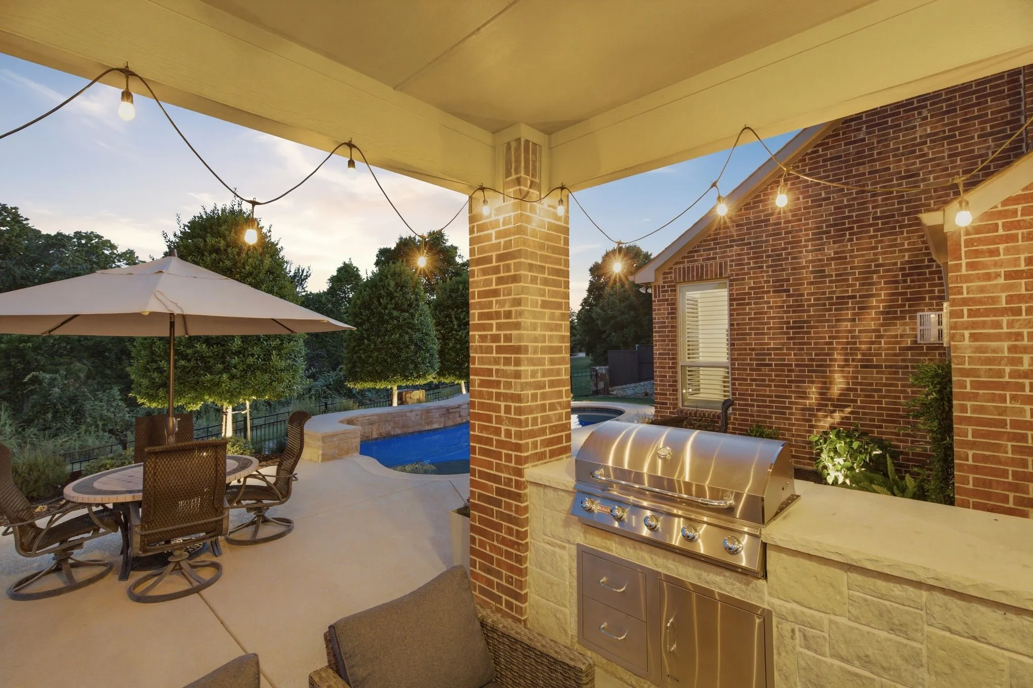 Covered outdoor patio featuring a built-in stainless steel grill, stone veneer base, and string lighting