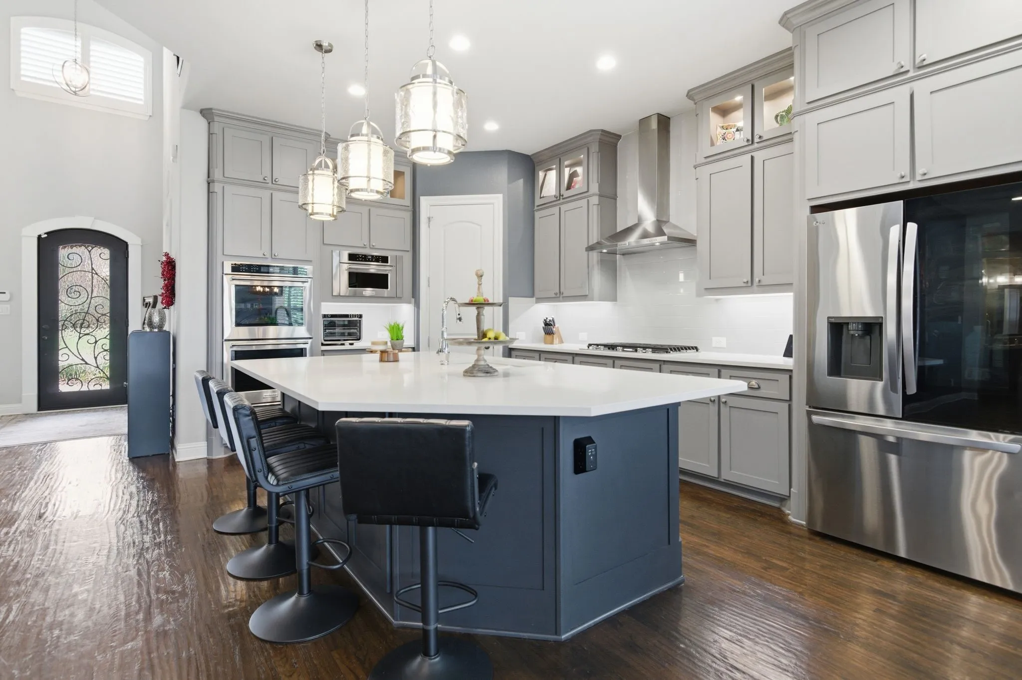 Gourmet kitchen featuring a large central island with seating, stainless steel appliances, extensive cabinetry, light countertops, and dark wood-finish flooring