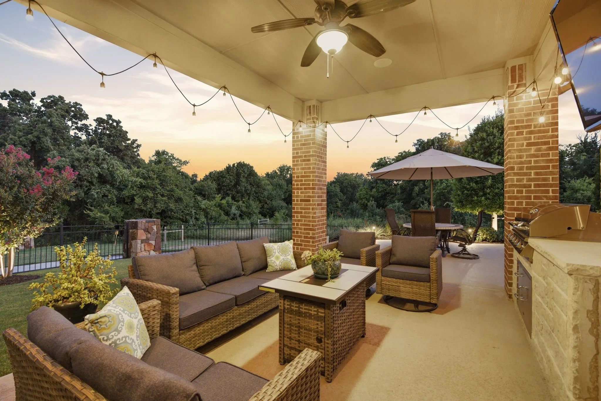 Expansive covered patio featuring a built-in outdoor kitchen, brick pillars, string lighting, and an integrated ceiling fan