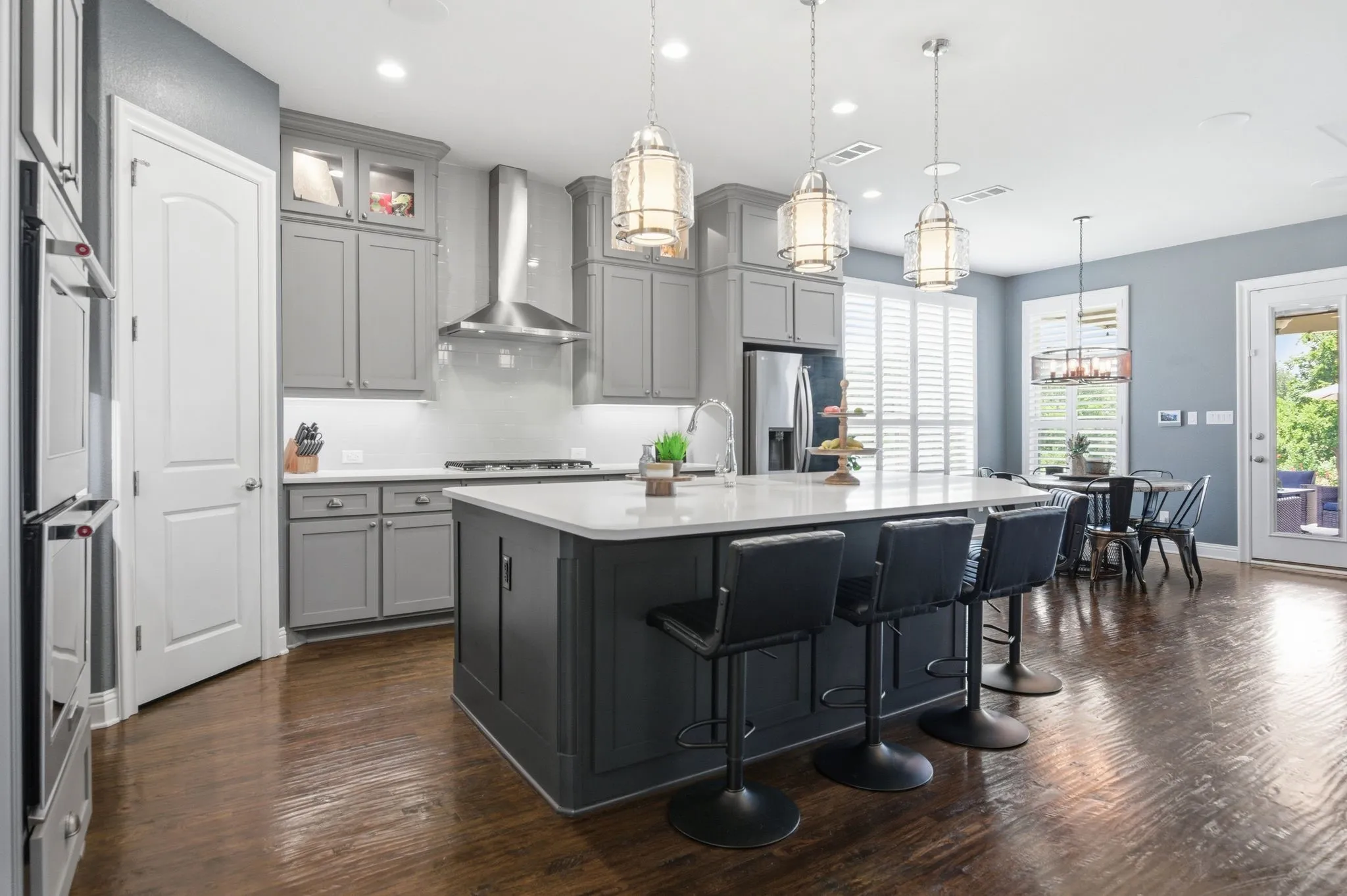 Kitchen featuring an island with white countertop, grey cabinetry, stainless steel appliances, wood-finish flooring, and pendant lighting