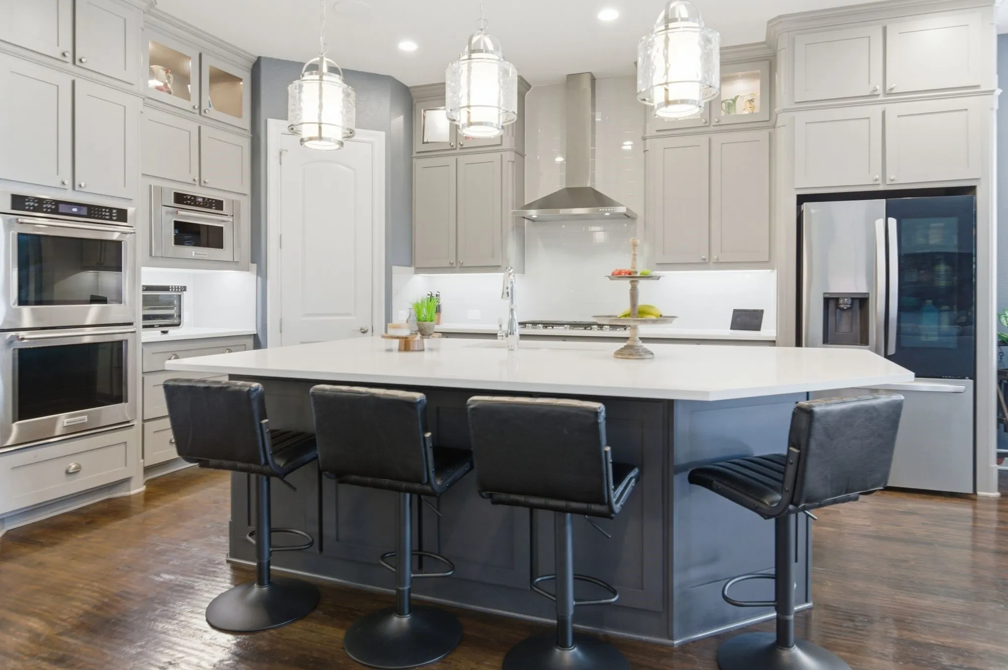 Kitchen featuring a large central island with a white countertop and dark gray base, stainless steel wall ovens, a stainless steel microwave, and a stainless steel refrigerator