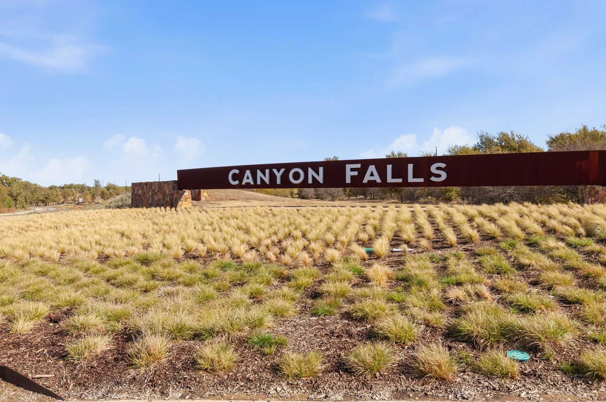 Community entry sign with a weathered steel finish and stone base, set against a backdrop of natural landscaping with ornamental grasses and mature trees
