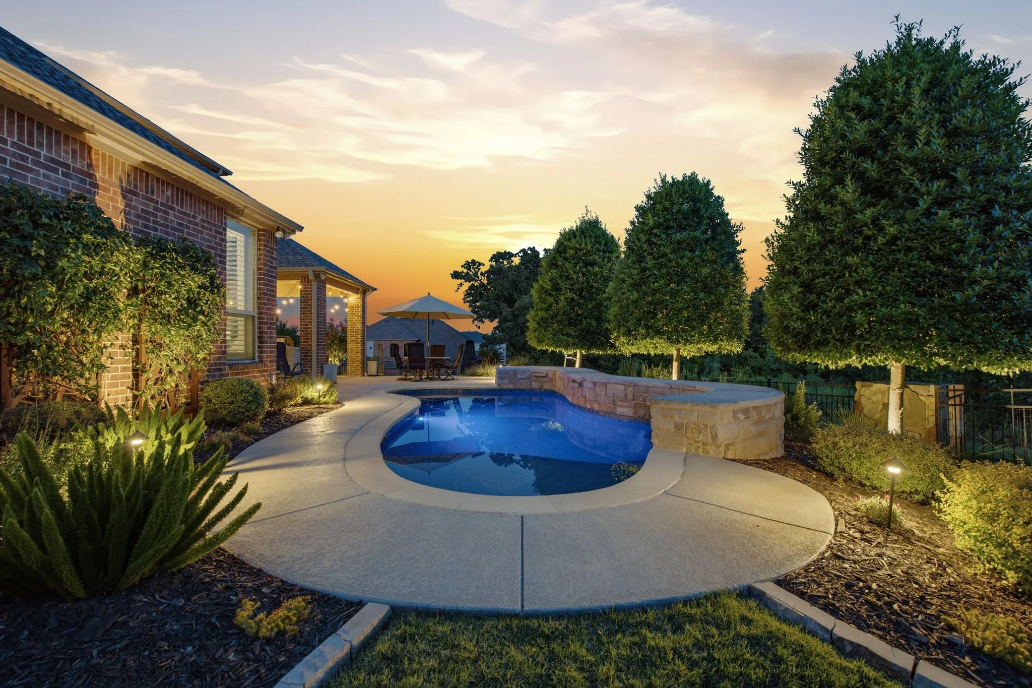 Curved swimming pool with an integrated stone spa, surrounded by concrete decking and landscaped borders
