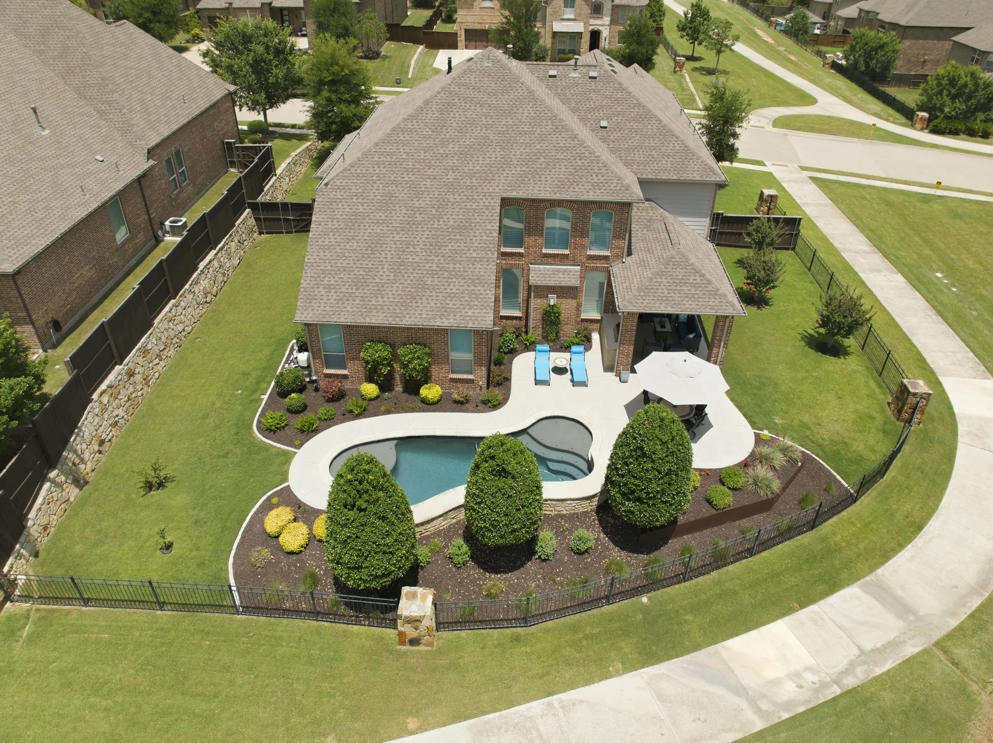 Brick exterior with a gabled roof, custom-shaped swimming pool, paved patio, and covered outdoor living area