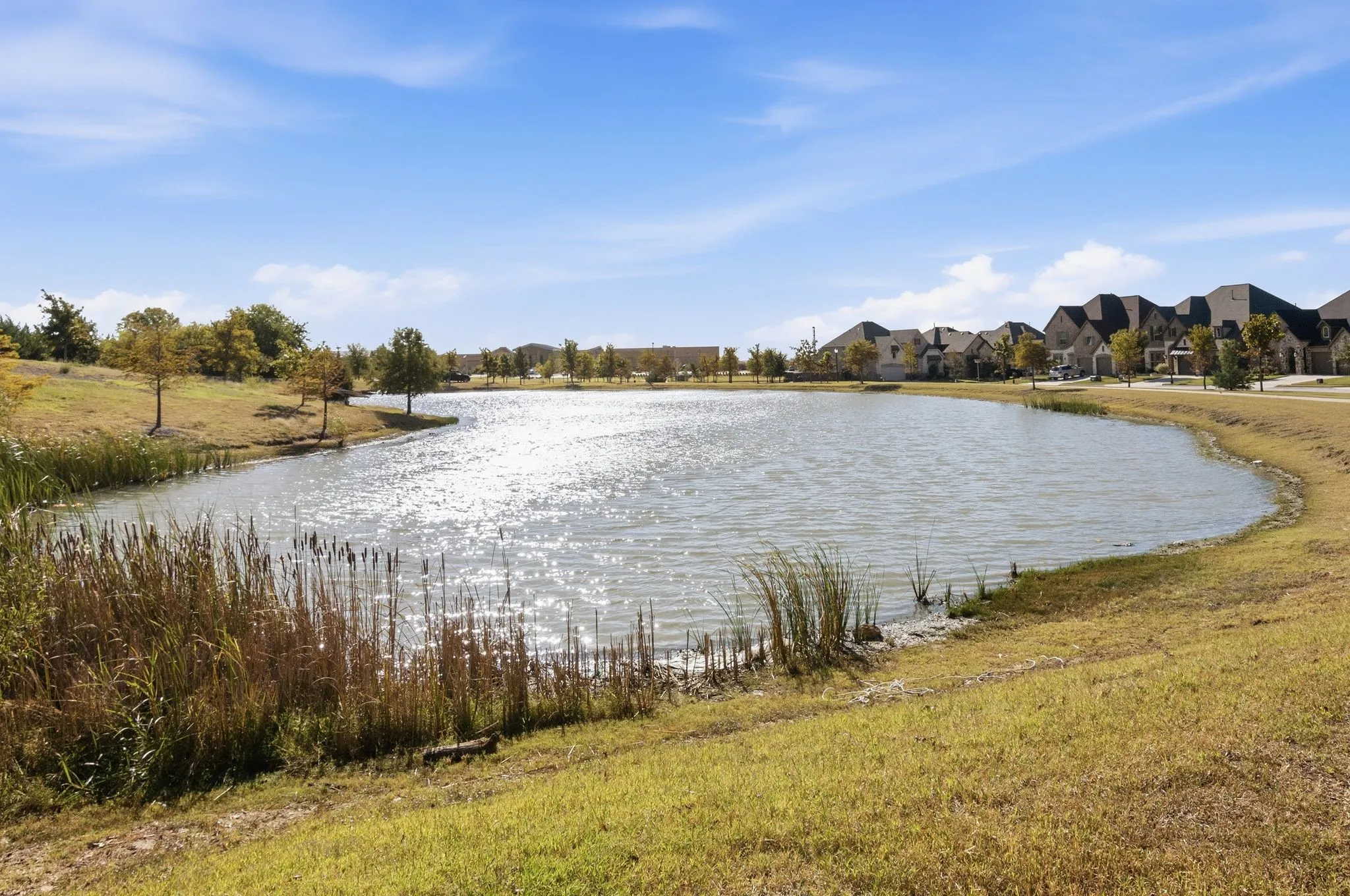 Water feature with natural bank, surrounding green space, and distant residential structures
