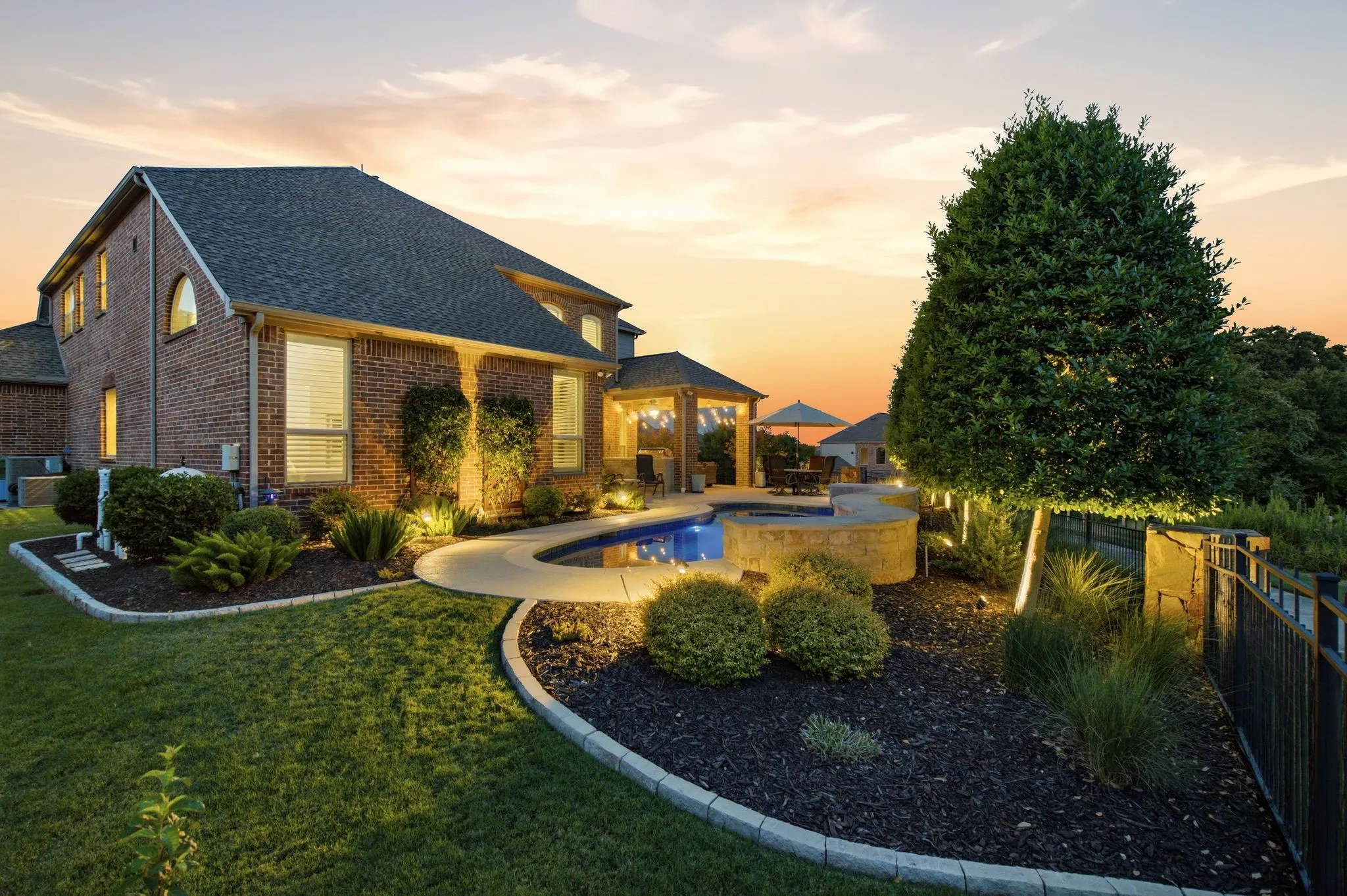 Brick exterior residence featuring a curved swimming pool, integrated hot tub, and an outdoor pavilion with a dining area