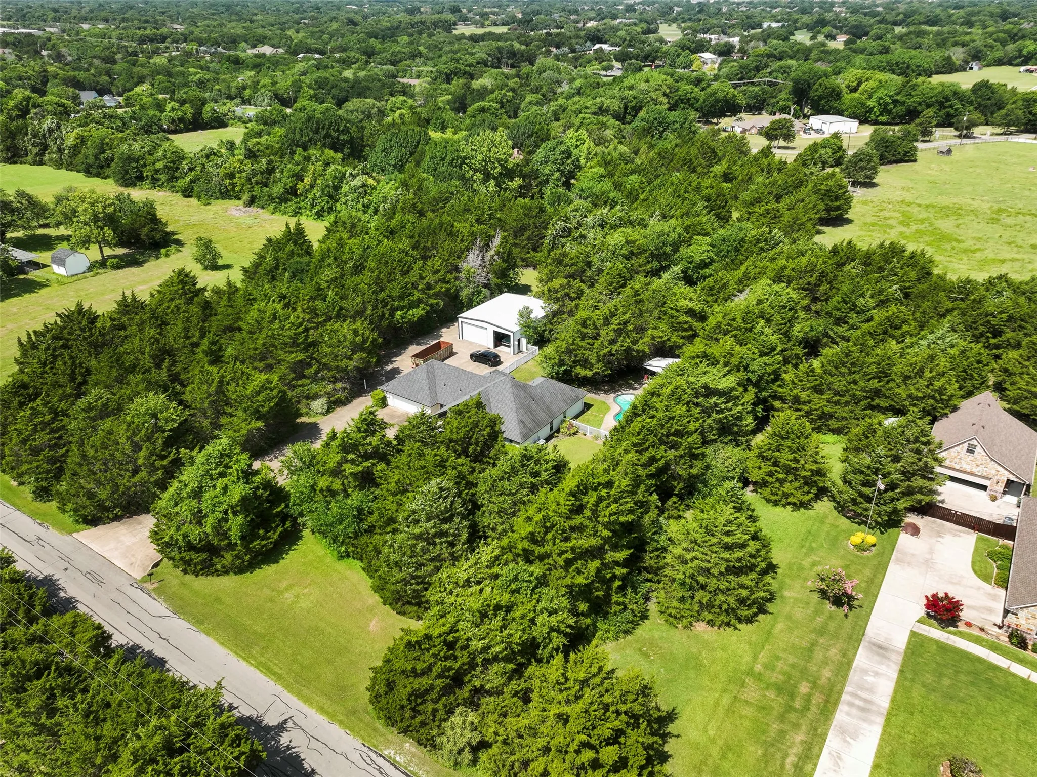 Expansive wooded property featuring a residential structure with a dark roof, a detached auxiliary building with a light-colored roof, and an in-ground swimming pool