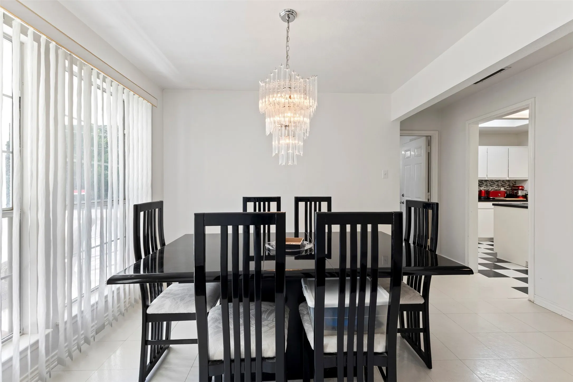 Dining area featuring a tiered crystal chandelier, expansive windows with vertical blinds, and a white tile floor