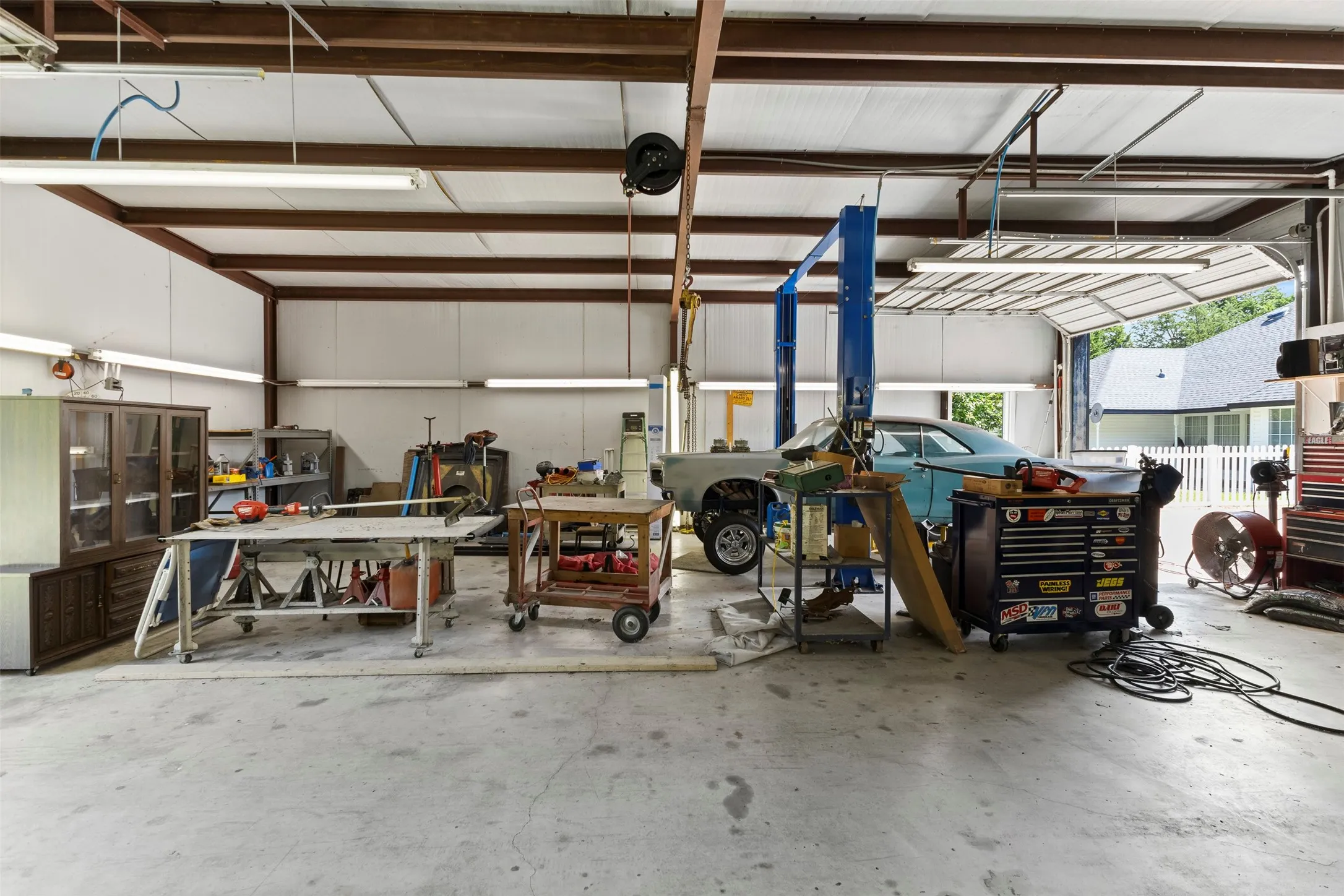 34x40 Spacious workshop featuring a concrete floor, metal beam construction, multiple fluorescent light fixtures, and a vehicle lift