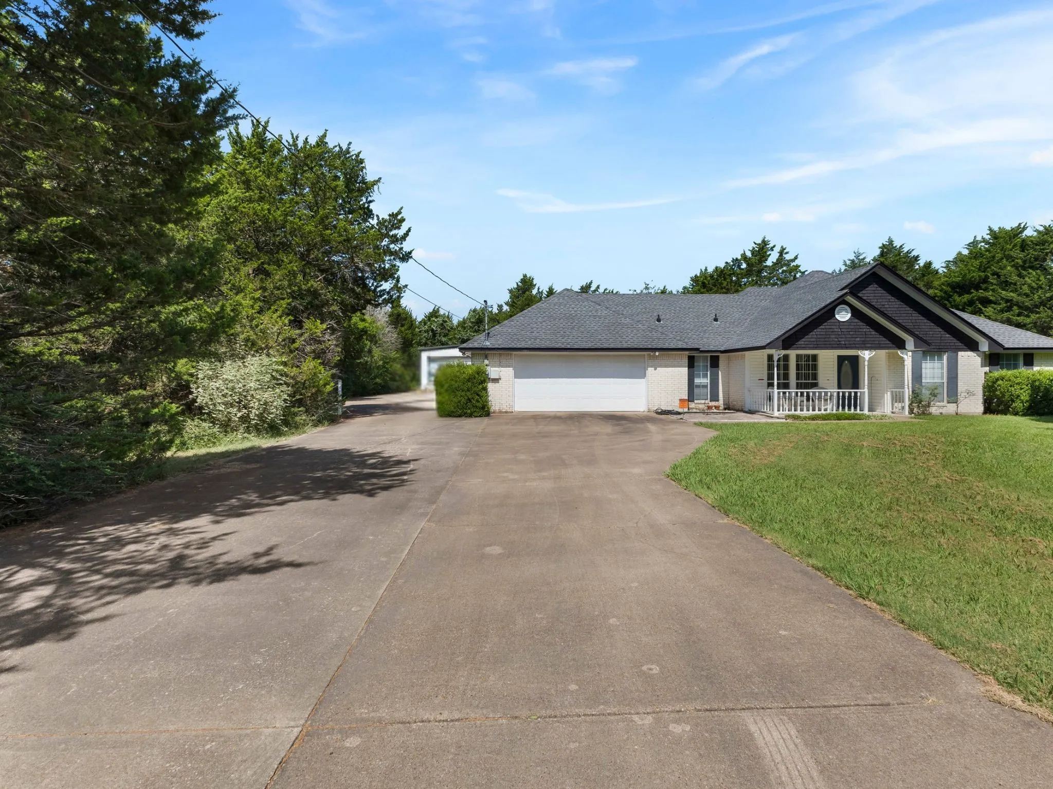 Spacious concrete driveway and front yard with mature landscaping