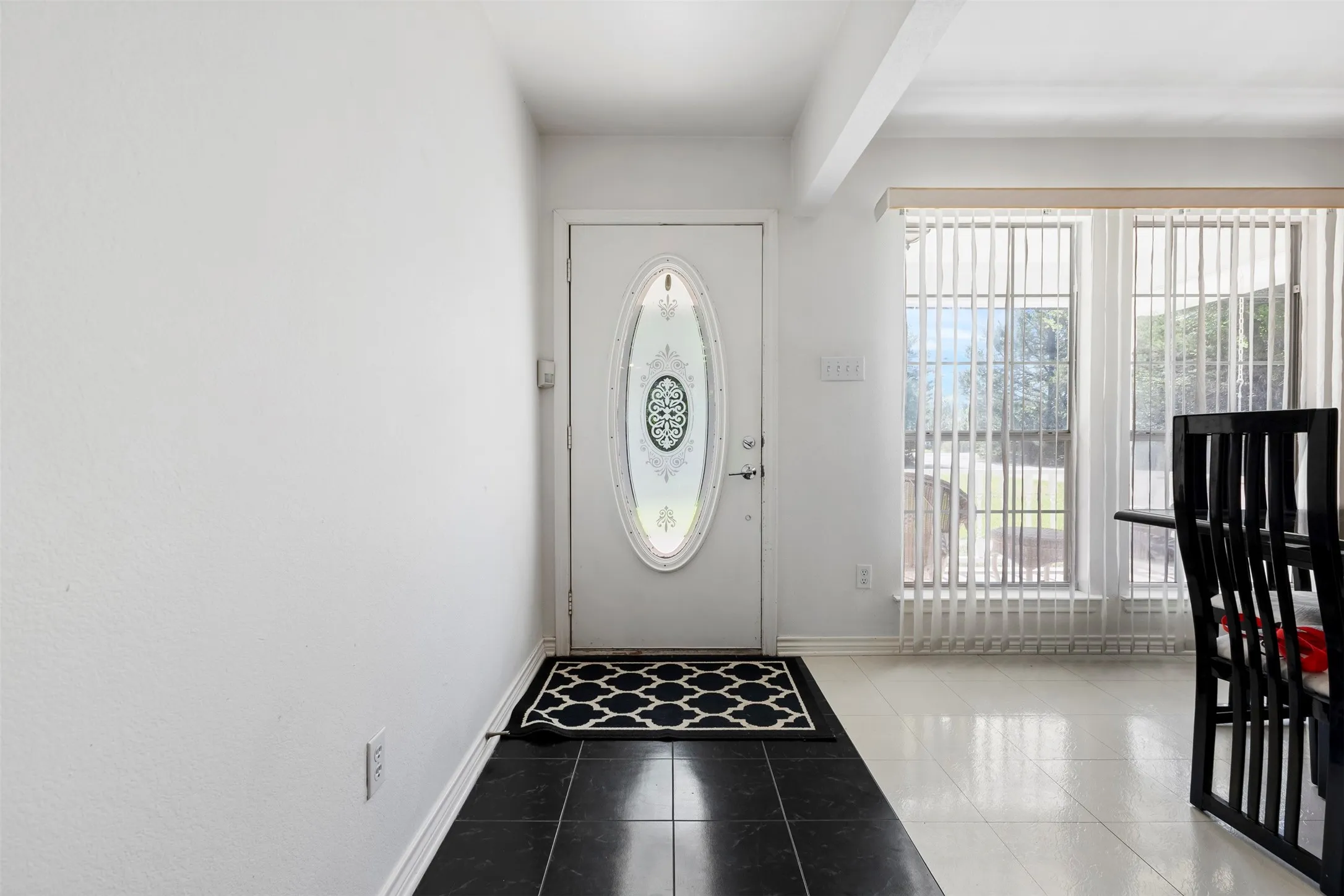 Entryway featuring a decorative oval-inset front door, black tile flooring, and white baseboards