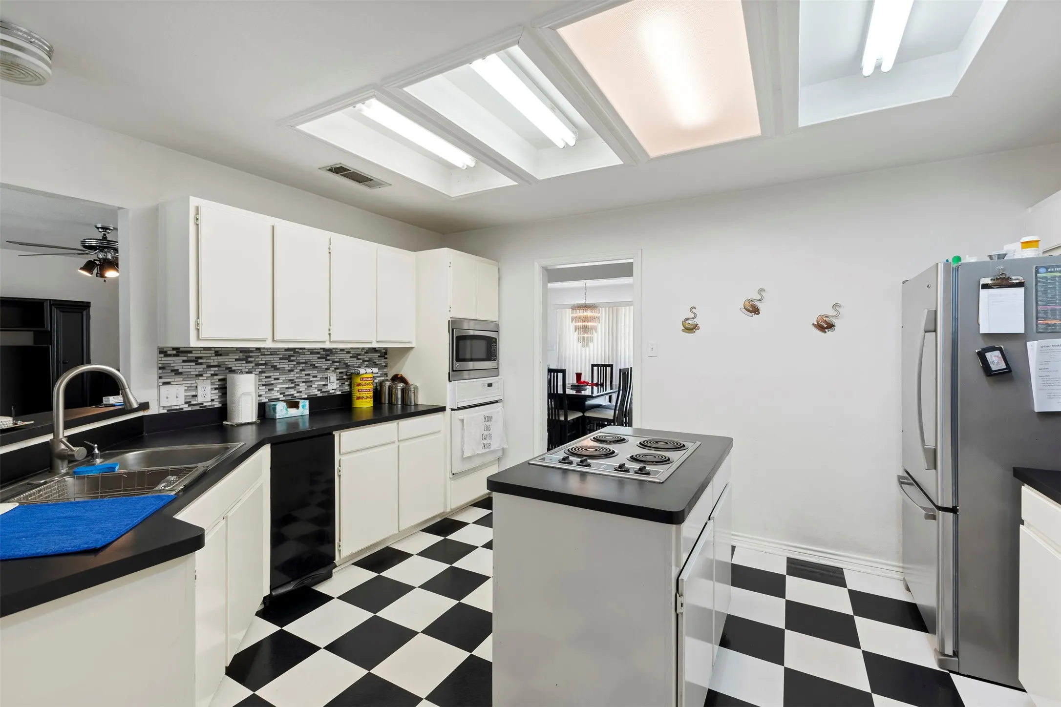 Kitchen featuring black and white checkerboard flooring, white cabinetry, black countertops, and a tile backsplash