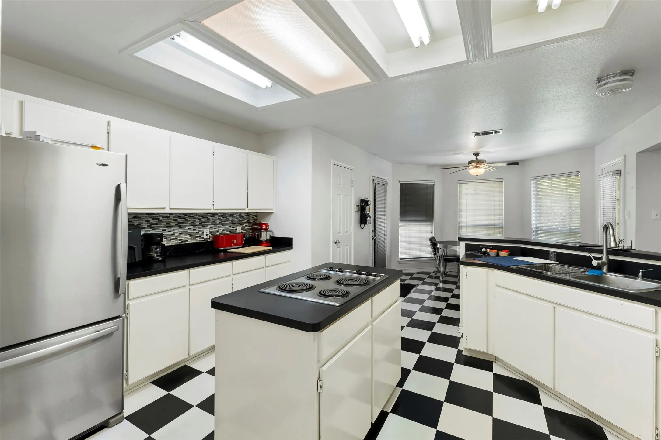 Kitchen featuring black and white checkerboard flooring, white cabinetry, black countertops, and a mosaic tile backsplash