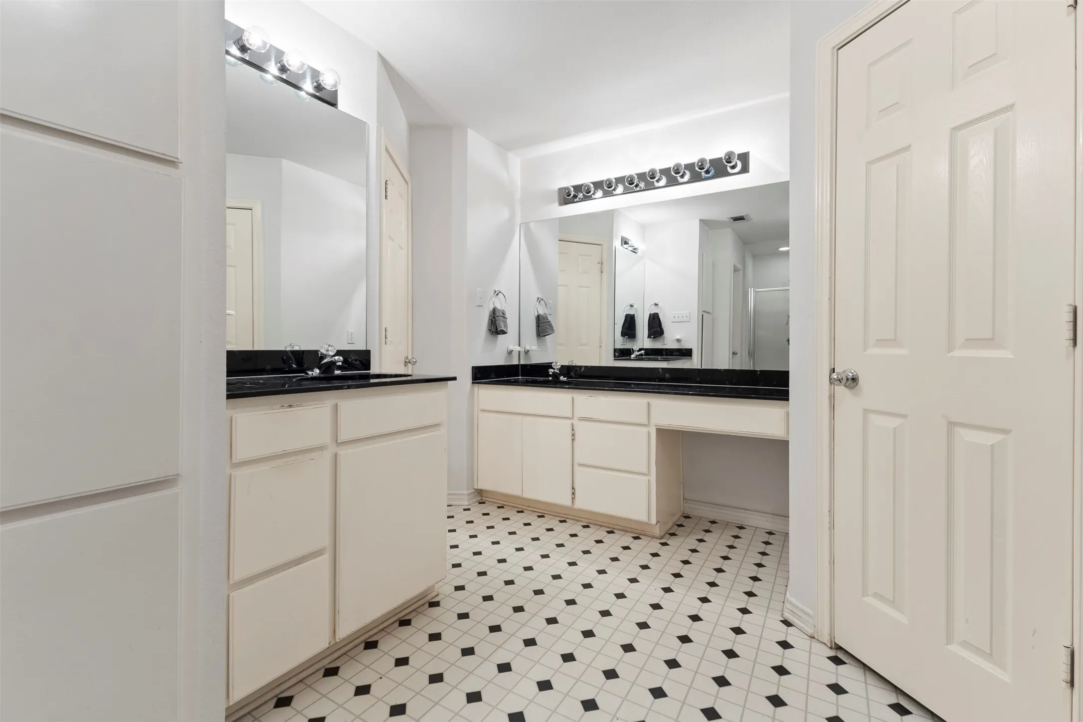 Bathroom featuring a black and white geometric tile floor, two separate vanity cabinets with sinks, dark countertops, and wall-mounted light fixtures