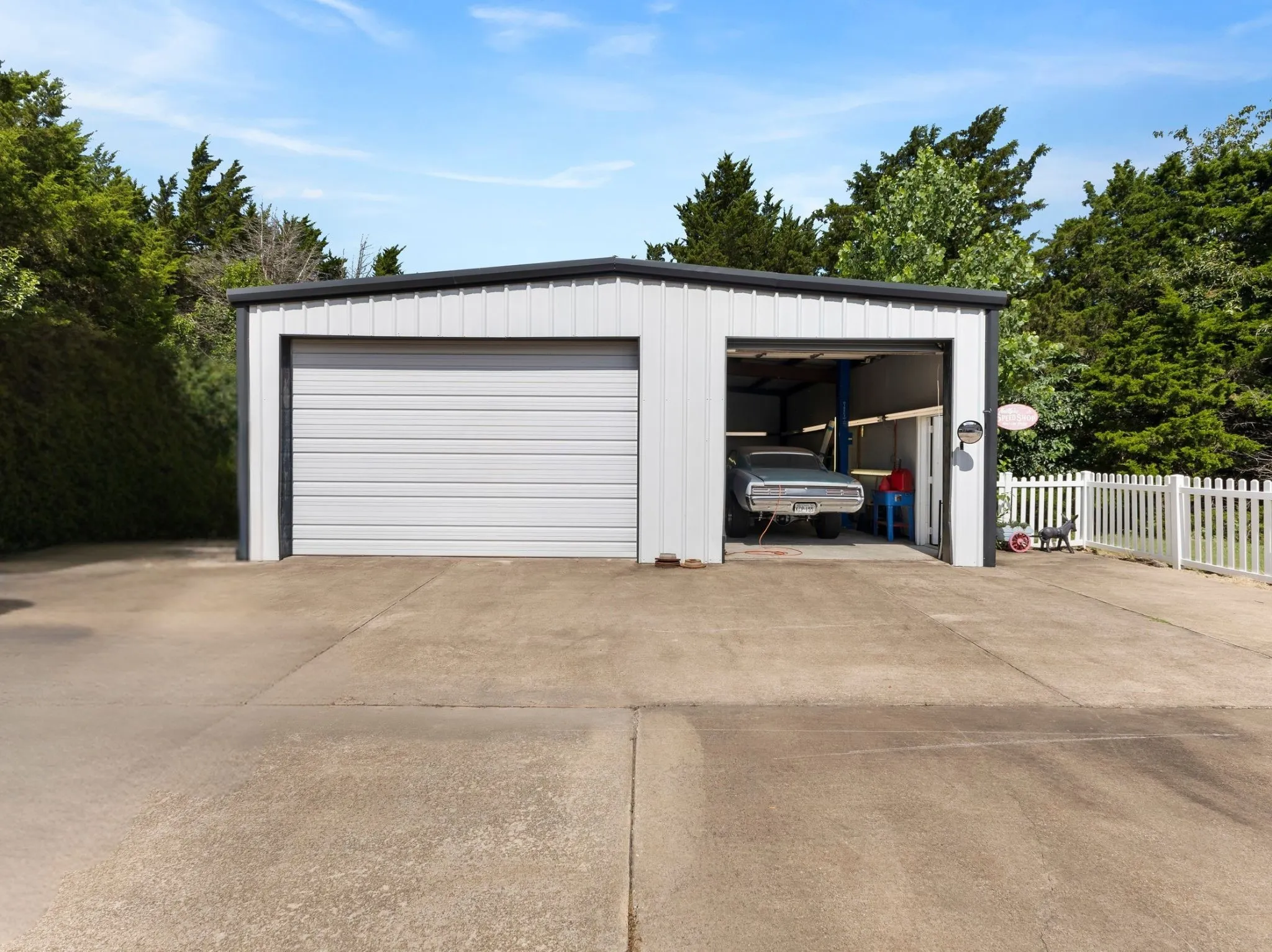 Two-bay metal garage structure featuring a roll-up door and an open bay with a lift system