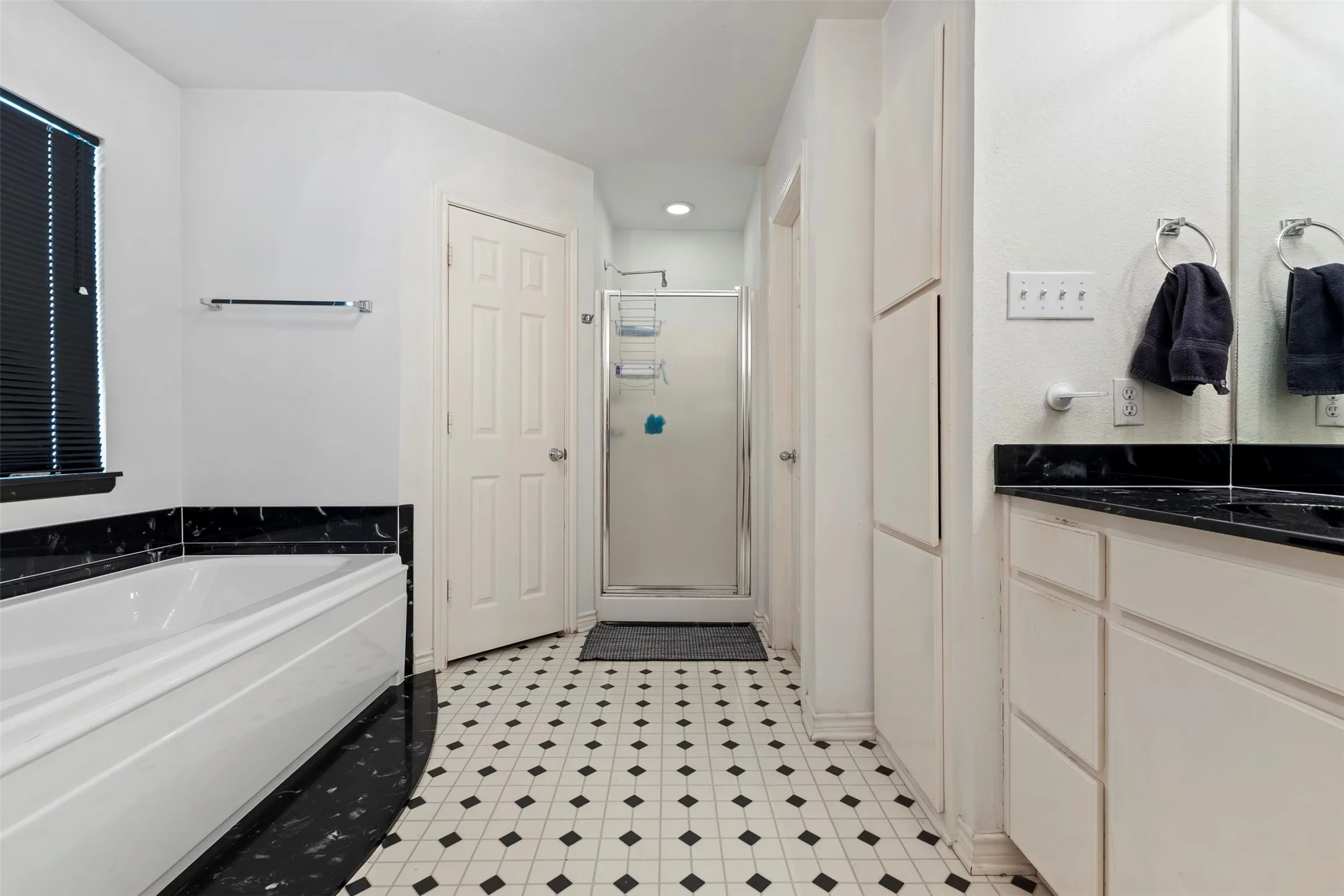 Bathroom featuring a shower enclosure, a bathtub with a black marble surround, and an extensive vanity with a black countertop and dual sinks