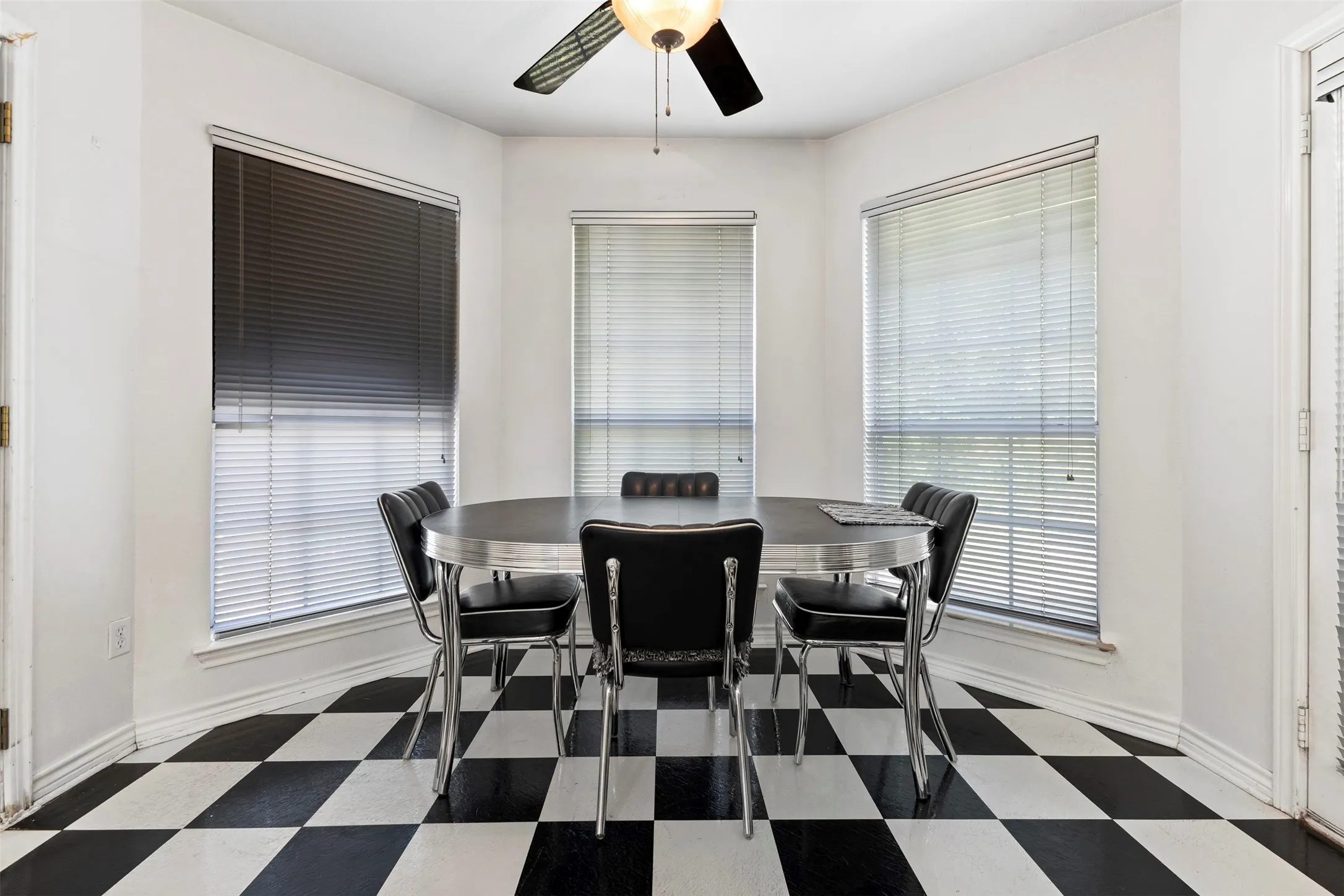 Breakfast nook featuring a bay window, black and white checkered flooring, and a ceiling fan