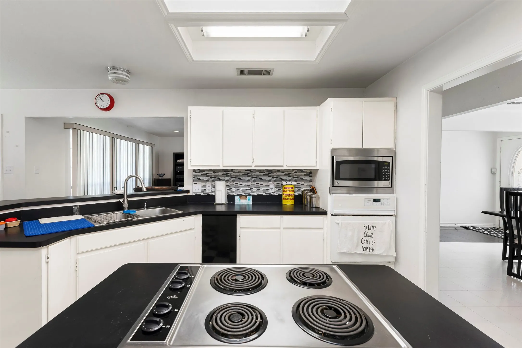 Kitchen featuring an island cooktop, white cabinetry, black countertops, and a mosaic tile backsplash