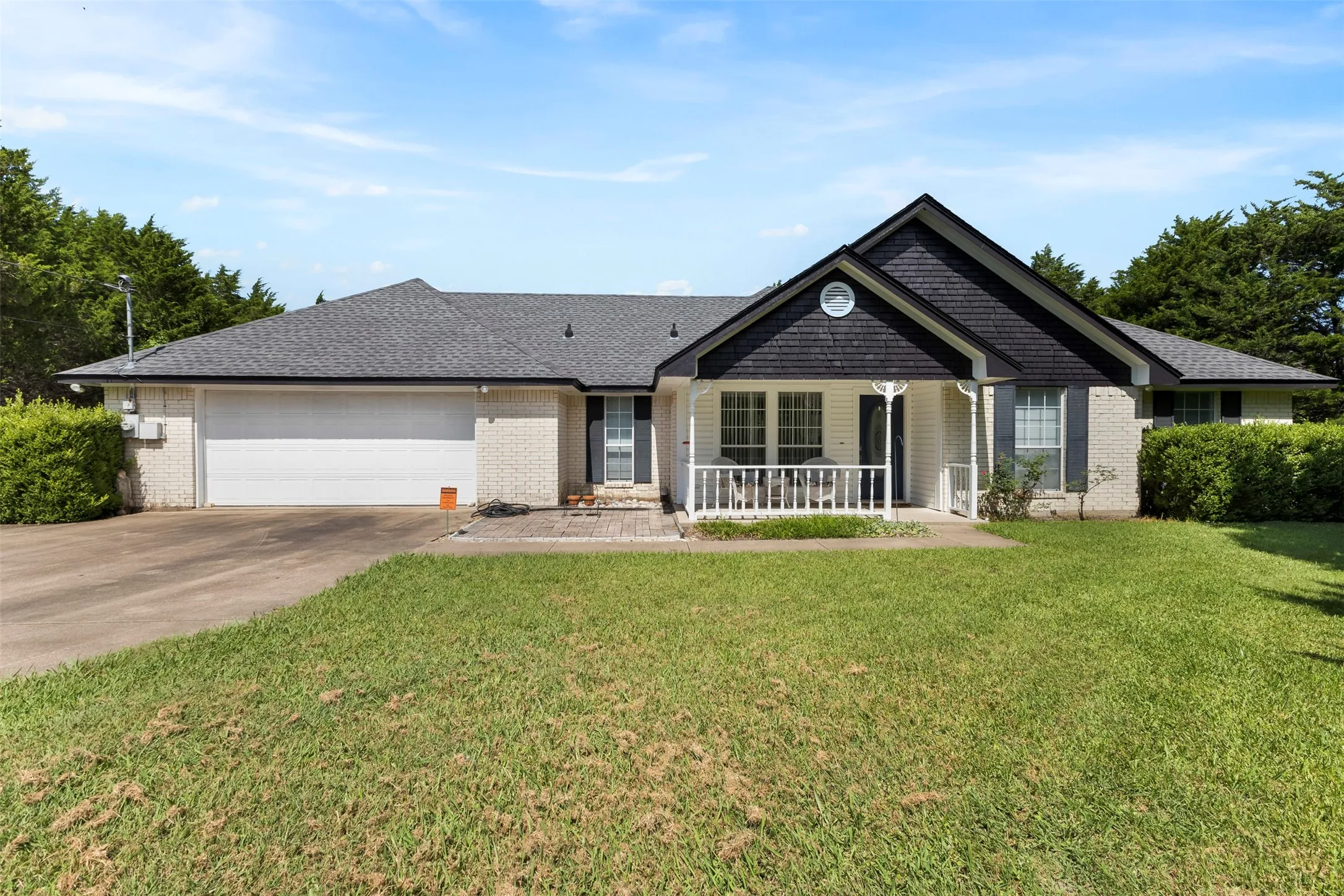 Ranch-style residence featuring a white brick facade, dark gray shingle roof, and a covered front porch with white railings