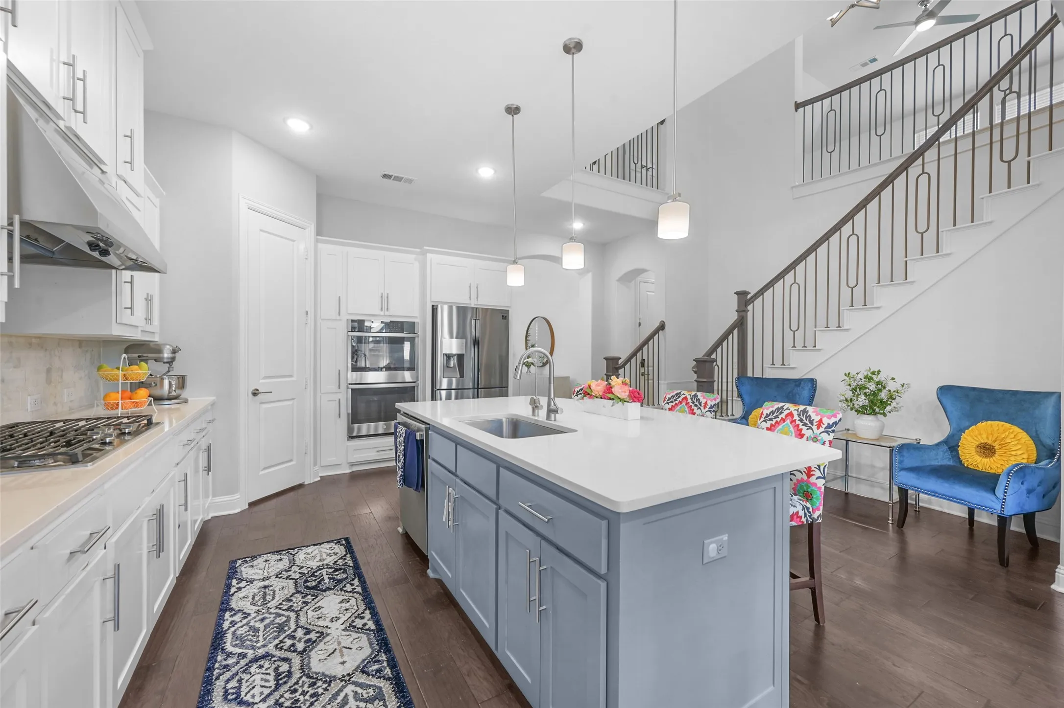 Kitchen with a central island featuring a sink and pendant lighting, stainless steel appliances, a gas range with an overhead exhaust hood, and wood-finish flooring