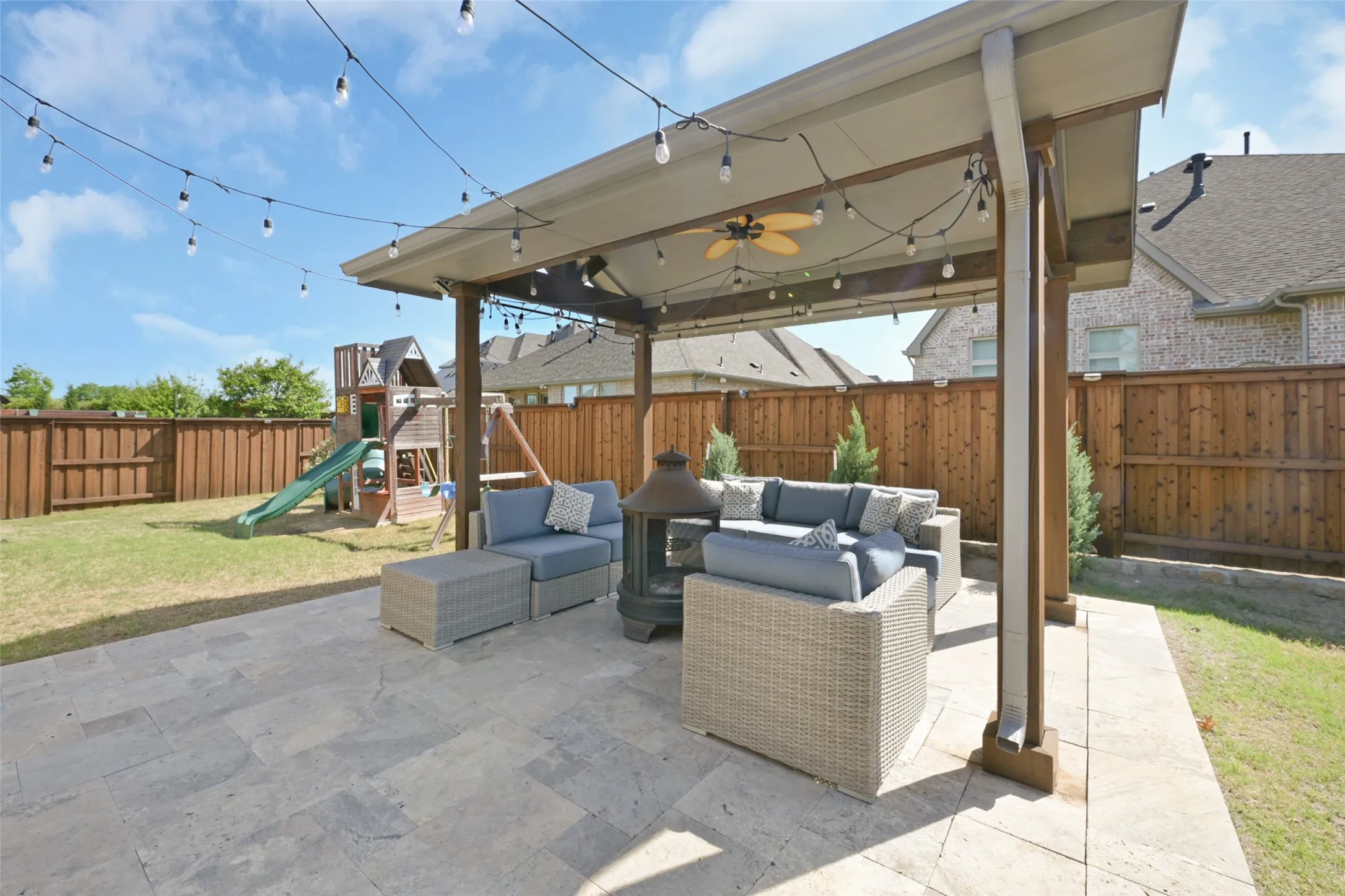 Expansive backyard featuring a stone patio and a covered pergola with a ceiling fan