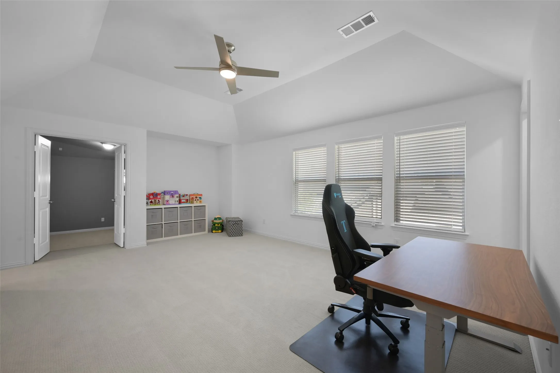 Spacious room featuring vaulted ceilings, light-colored carpeting, and three windows with horizontal blinds