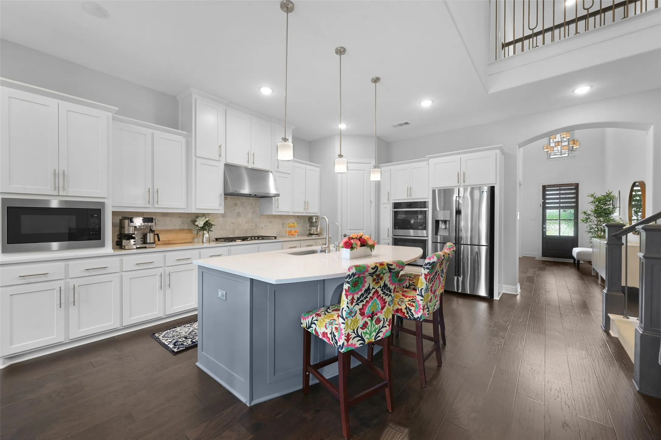 Open-concept kitchen featuring an island with counter seating, white shaker-style cabinetry, stainless steel appliances, and wood-finish flooring