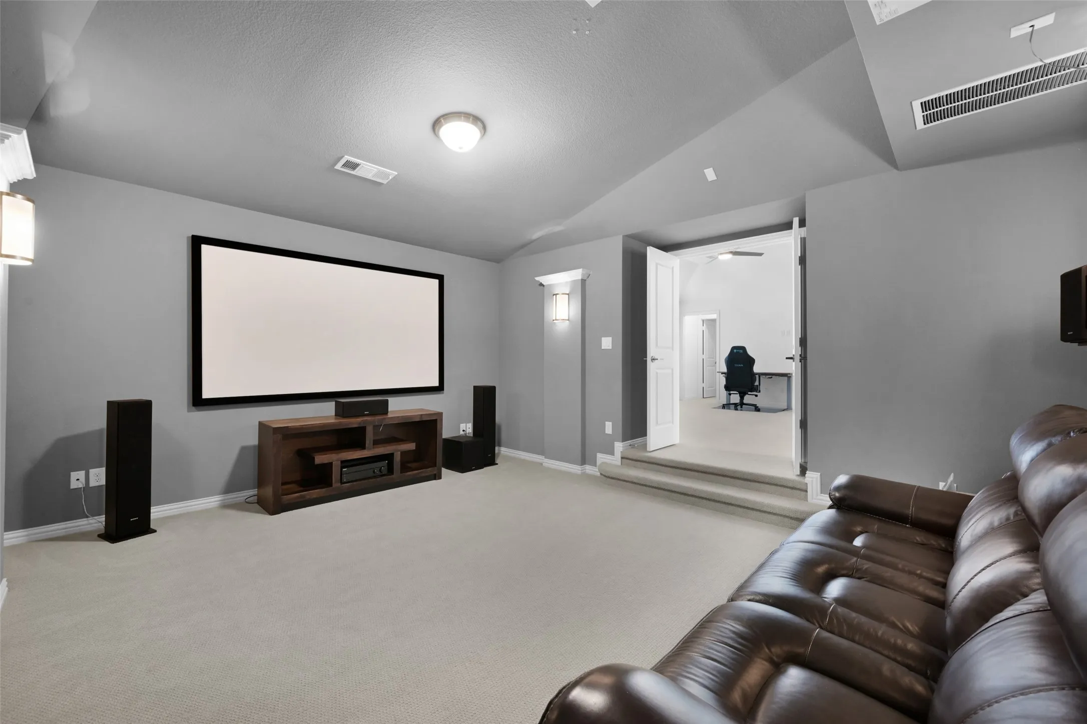 Dedicated media room featuring a large projector screen, recessed ceiling lighting, and wall sconces