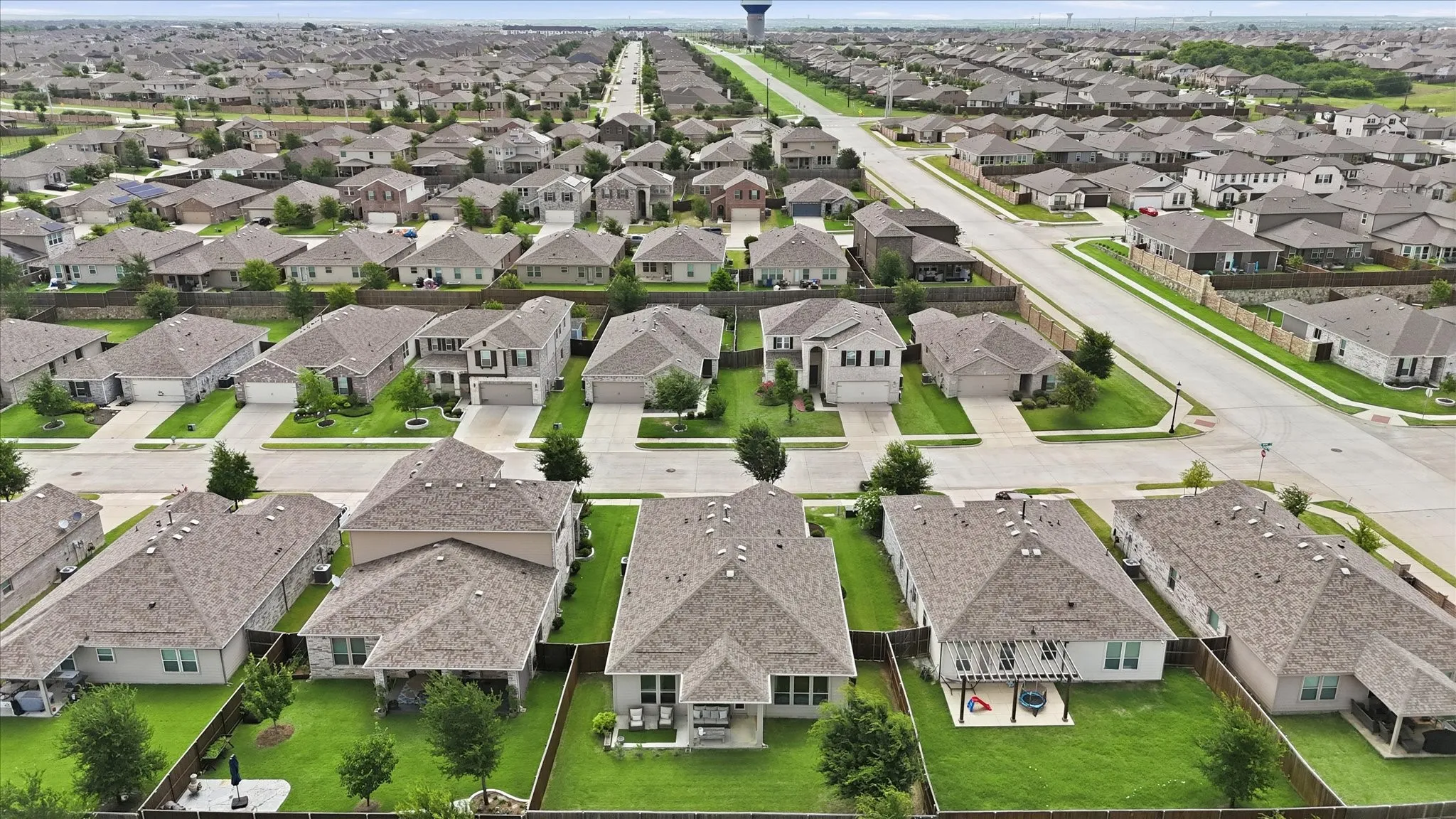 Aerial perspective showcasing a residential neighborhood with uniform single-family homes, each featuring a pitched roof, individual driveway, and a fenced backyard
